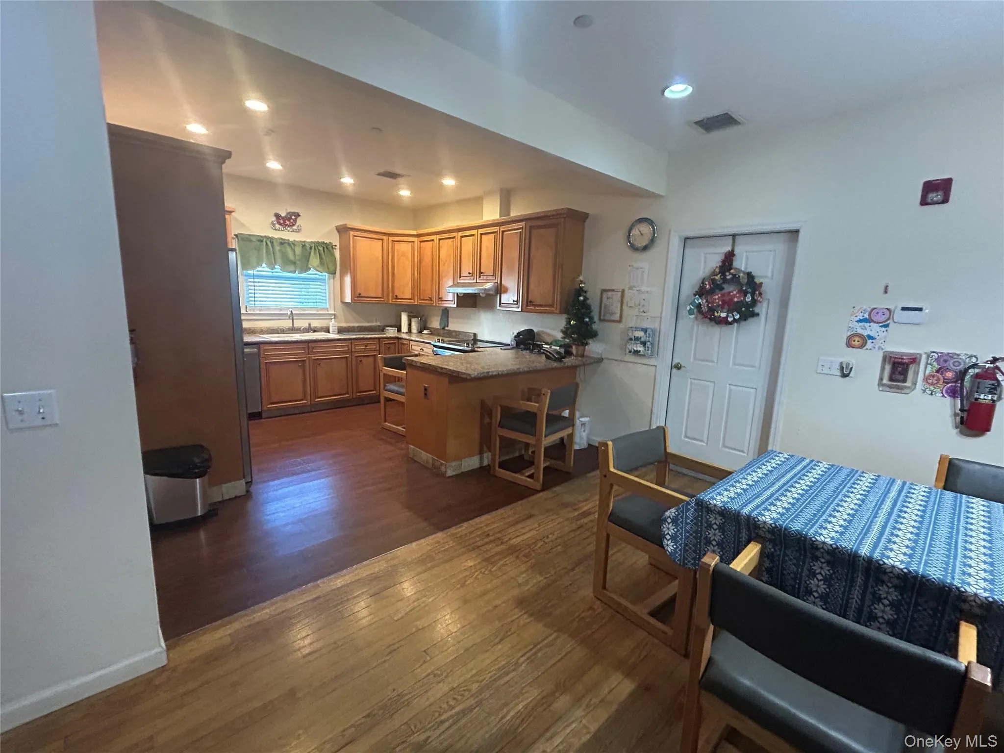 Kitchen with a peninsula, dark wood-style flooring, brown cabinets, recessed lighting, and a breakfast bar Kitchen with a peninsula, dark wood-style flooring, brown cabinets, recessed lighting, and a breakfast bar