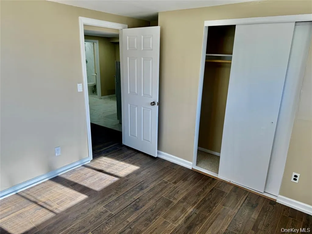 Wood-finish flooring, neutral wall color, white trim, sliding closet doors, and a six-panel interior door Wood-finish flooring, neutral wall color, white trim, sliding closet doors, and a six-panel interior door