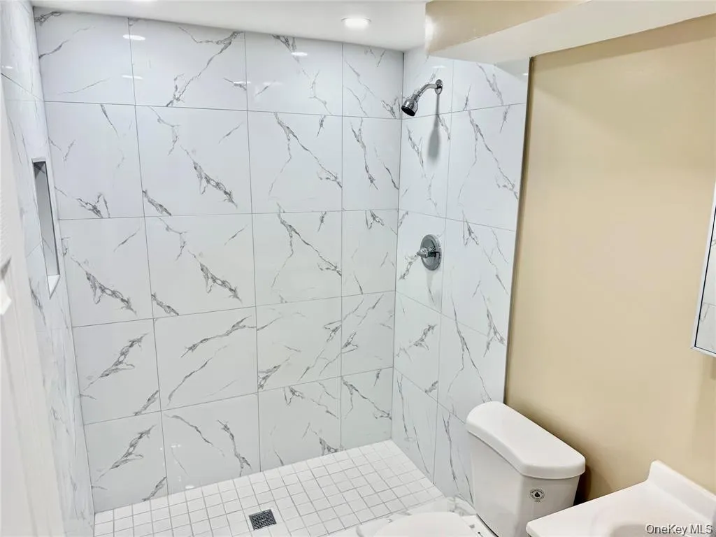 Shower with white marble-patterned tile, recessed shower niche, square tile shower base, and a chrome shower fixture Shower with white marble-patterned tile, recessed shower niche, square tile shower base, and a chrome shower fixture