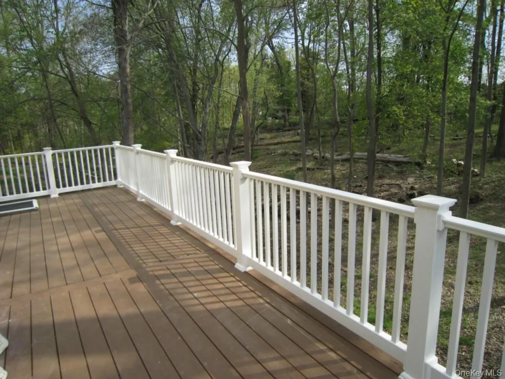 Expansive deck with wood-finish flooring and white railings, surrounded by mature trees Expansive deck with wood-finish flooring and white railings, surrounded by mature trees