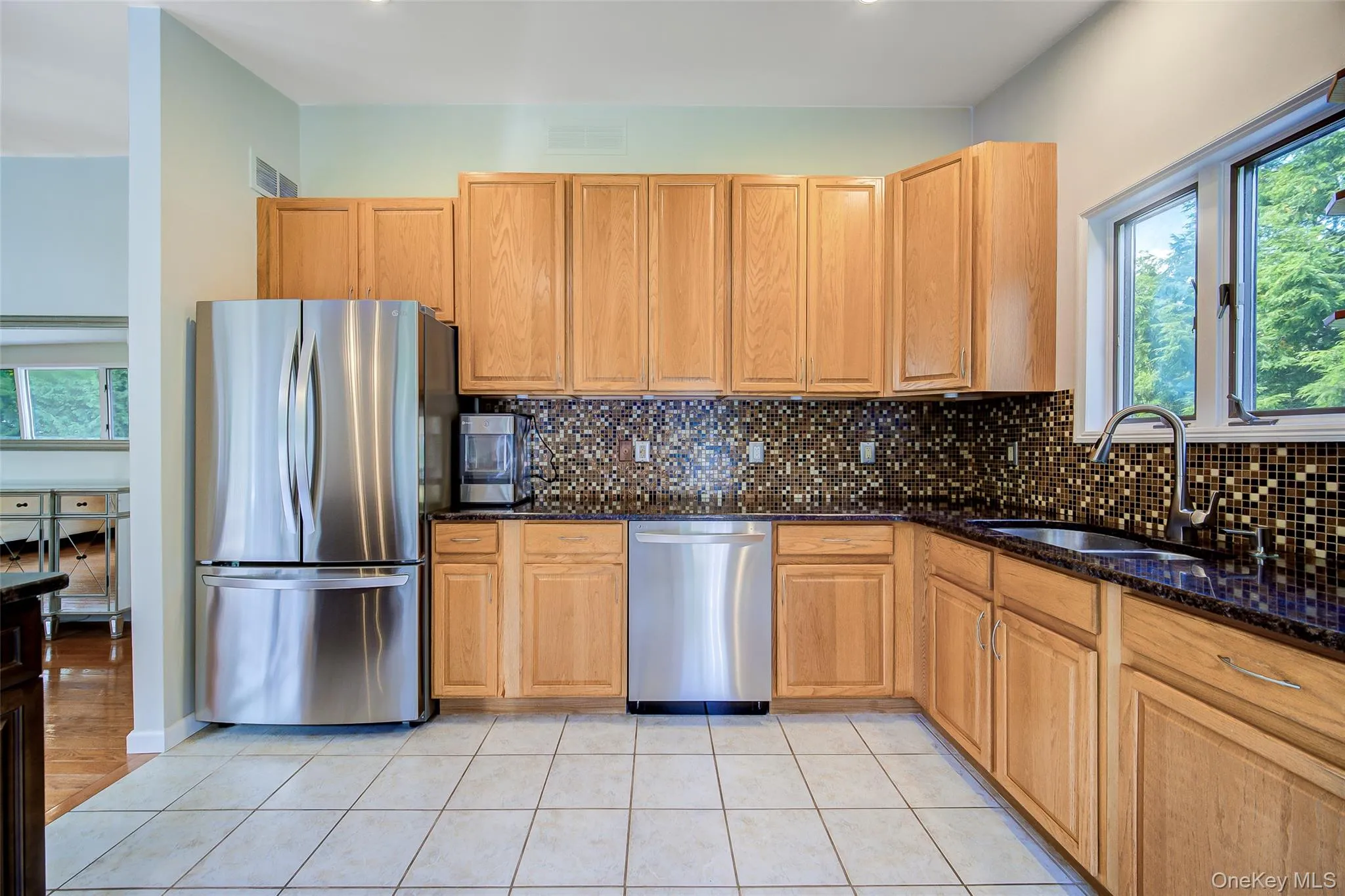 Kitchen featuring light-toned wood cabinetry, stainless steel appliances, dark countertops, and a mosaic tile backsplash Kitchen featuring light-toned wood cabinetry, stainless steel appliances, dark countertops, and a mosaic tile backsplash