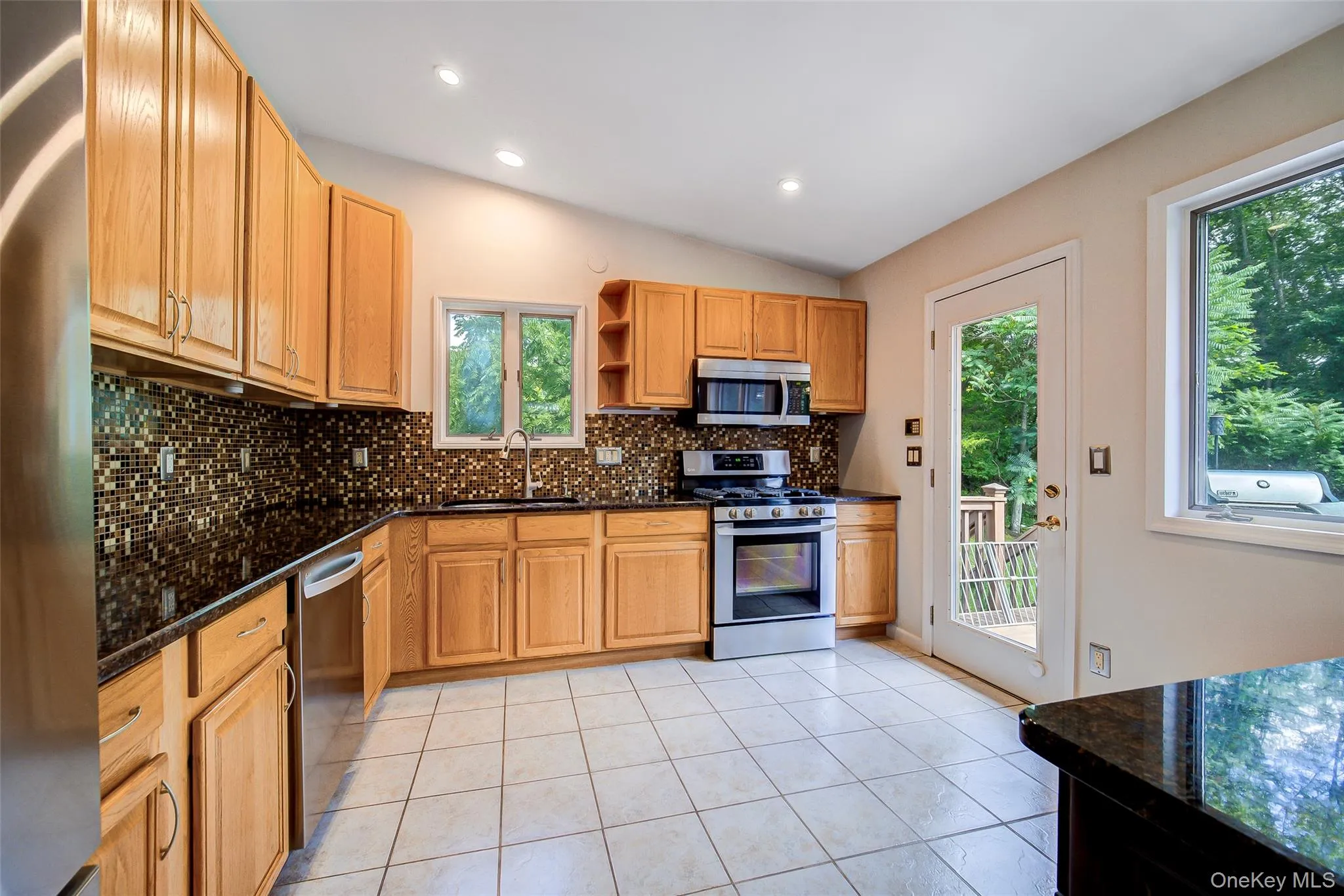 Kitchen featuring stainless steel appliances, dark countertops, tiled backsplash, wooden cabinetry, and tiled flooring Kitchen featuring stainless steel appliances, dark countertops, tiled backsplash, wooden cabinetry, and tiled flooring