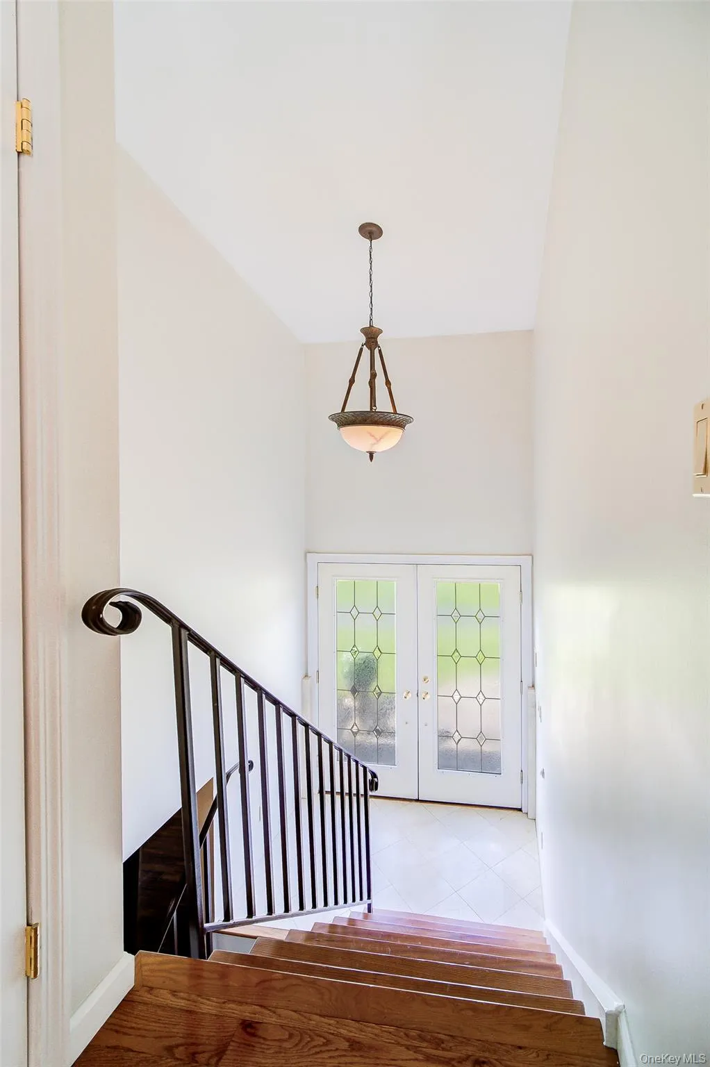 Hardwood-finish stairs with wrought iron railing, vaulted ceiling, and double paneled glass entry doors Hardwood-finish stairs with wrought iron railing, vaulted ceiling, and double paneled glass entry doors