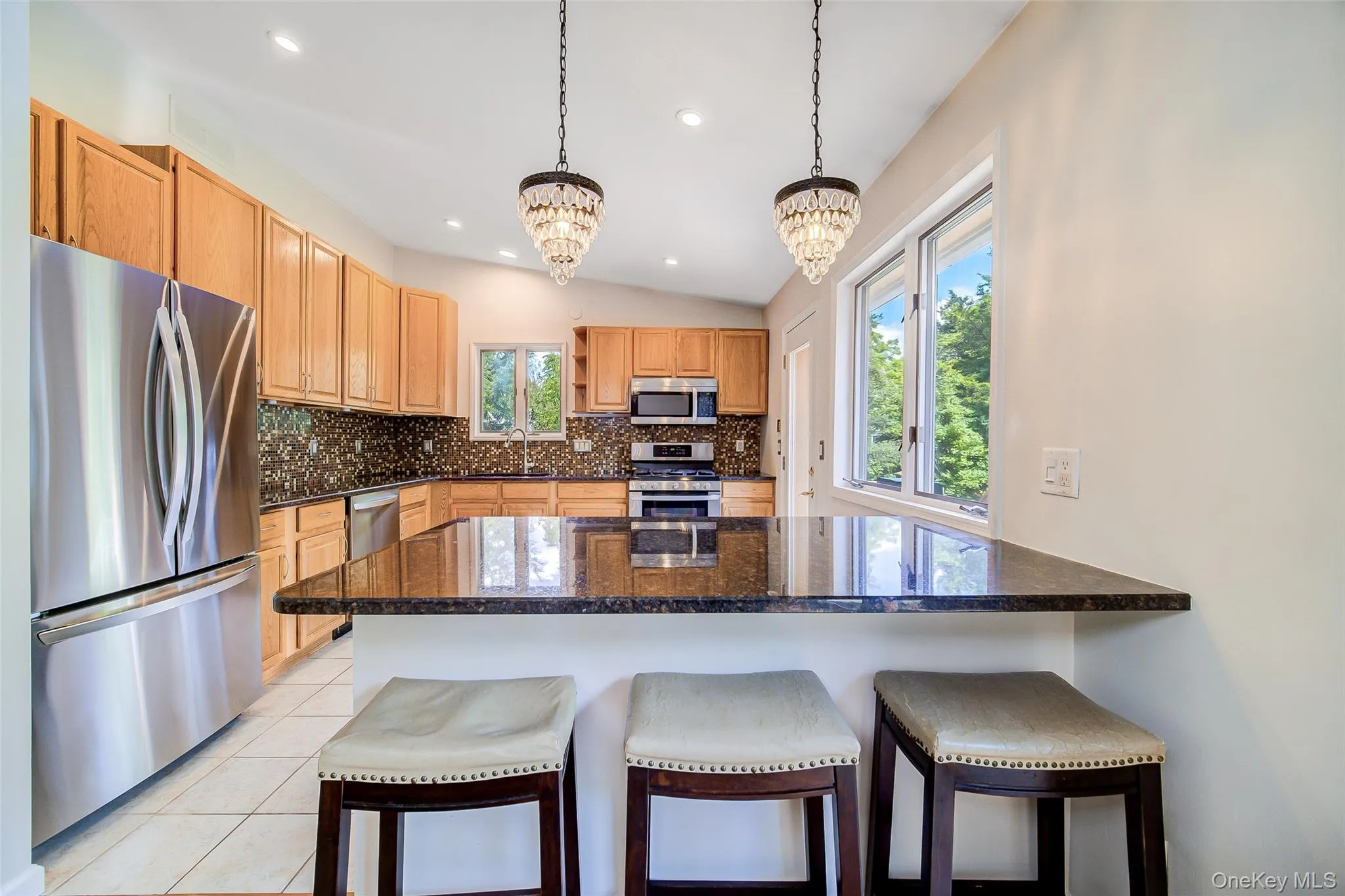 Kitchen featuring wood cabinetry, stainless steel appliances, a dark stone island, and dual pendant light fixtures Kitchen featuring wood cabinetry, stainless steel appliances, a dark stone island, and dual pendant light fixtures