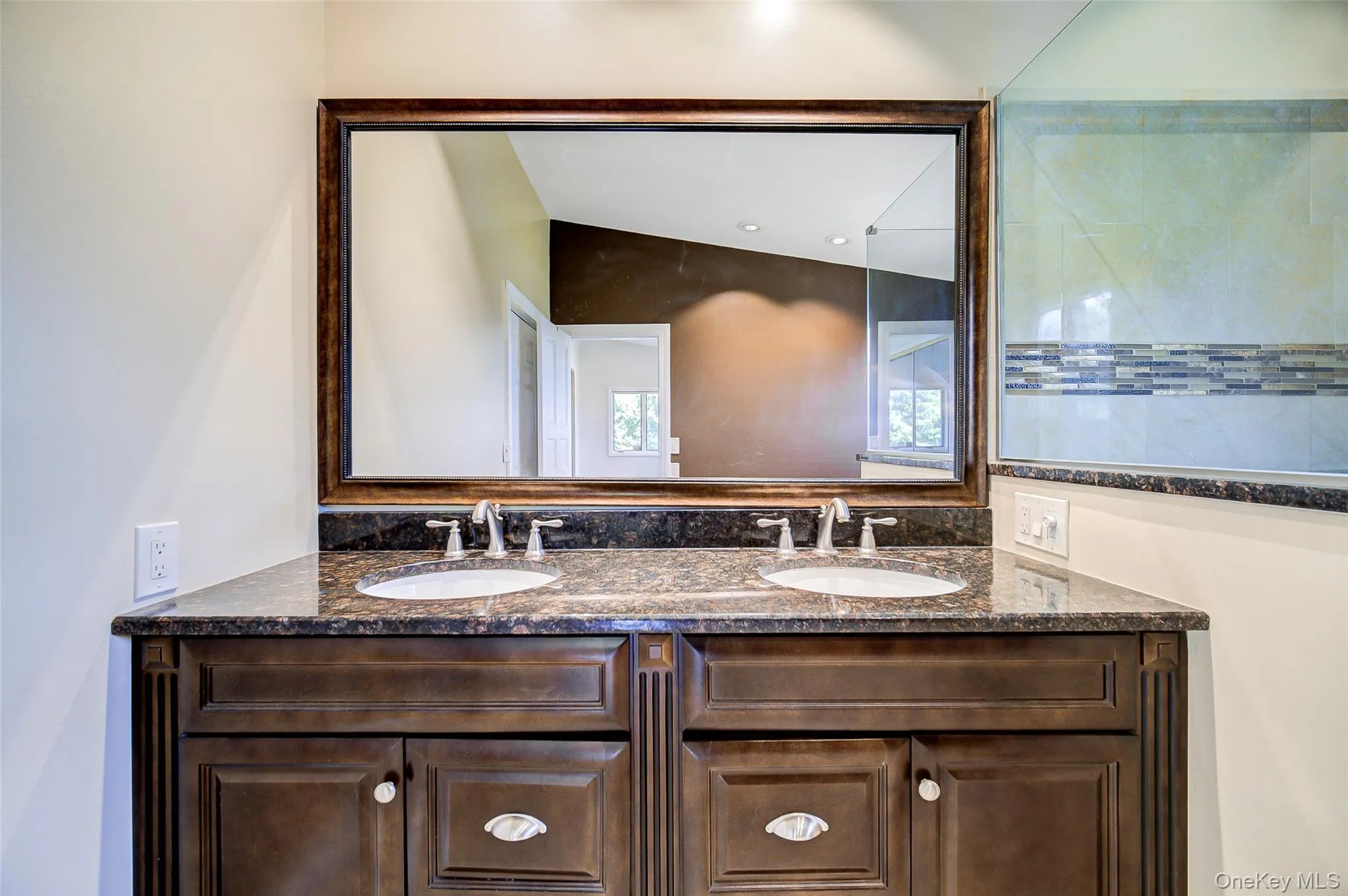 Double vanity with wood-finish cabinetry, dual undermount sinks, and a dark stone countertop Double vanity with wood-finish cabinetry, dual undermount sinks, and a dark stone countertop