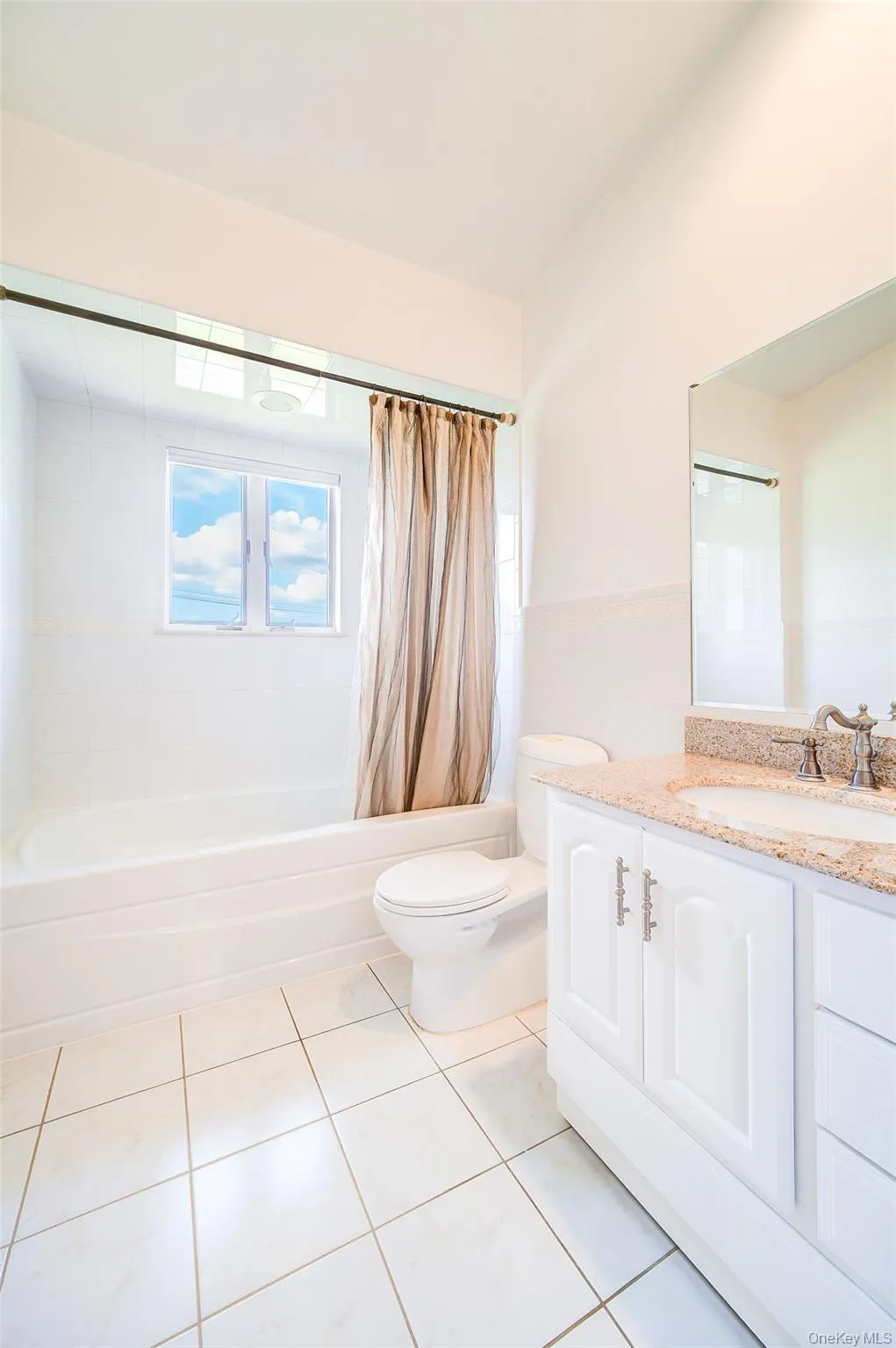 White tile flooring, white vanity with granite-style countertop, undermount sink, built-in tub, and window with natural light White tile flooring, white vanity with granite-style countertop, undermount sink, built-in tub, and window with natural light