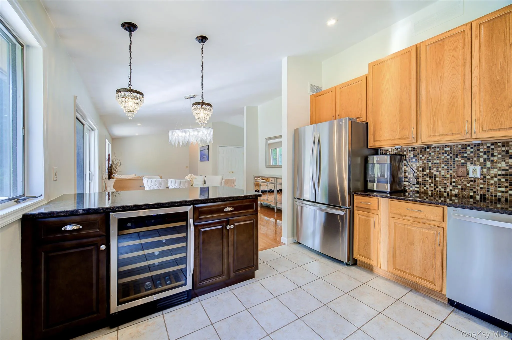 Kitchen featuring stainless steel appliances, dark stone countertops, mosaic tile backsplash, wood cabinetry, and a built-in beverage cooler Kitchen featuring stainless steel appliances, dark stone countertops, mosaic tile backsplash, wood cabinetry, and a built-in beverage cooler