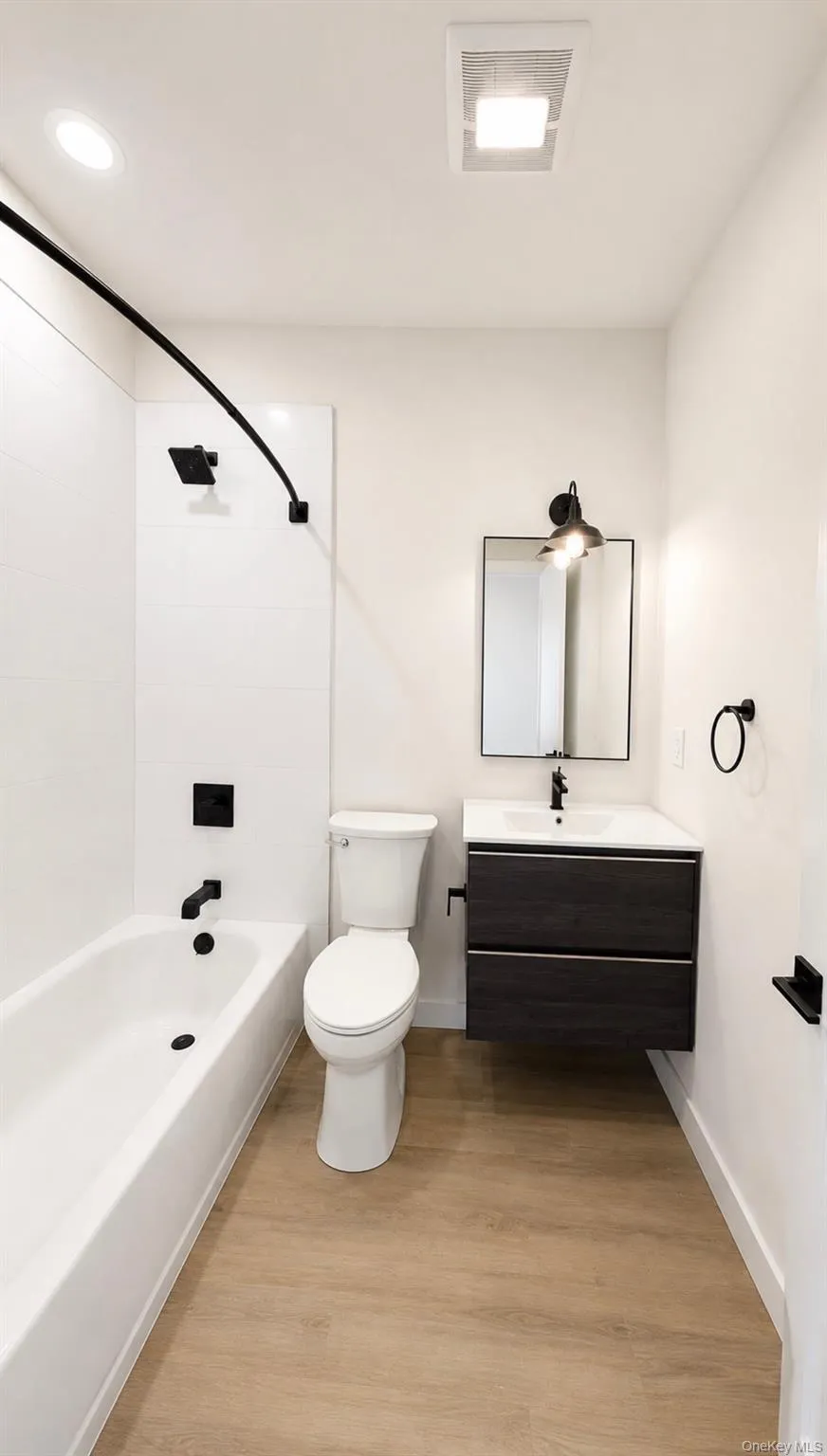 Wood-finish flooring, white subway tile shower surround, black-finish fixtures, floating vanity with integrated sink, and recessed lighting Wood-finish flooring, white subway tile shower surround, black-finish fixtures, floating vanity with integrated sink, and recessed lighting