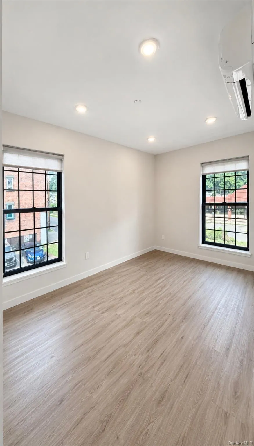 Recessed lighting, wood-finish flooring, two large windows, white walls, and a wall-mounted climate control unit Recessed lighting, wood-finish flooring, two large windows, white walls, and a wall-mounted climate control unit