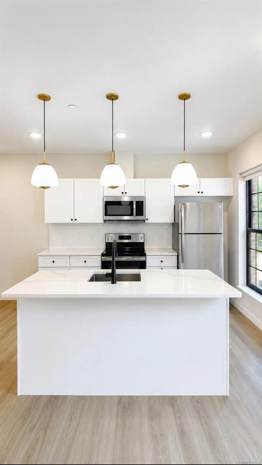 Kitchen featuring a central island with an undermount sink, quartz countertops, and wood-finish flooring Kitchen featuring a central island with an undermount sink, quartz countertops, and wood-finish flooring