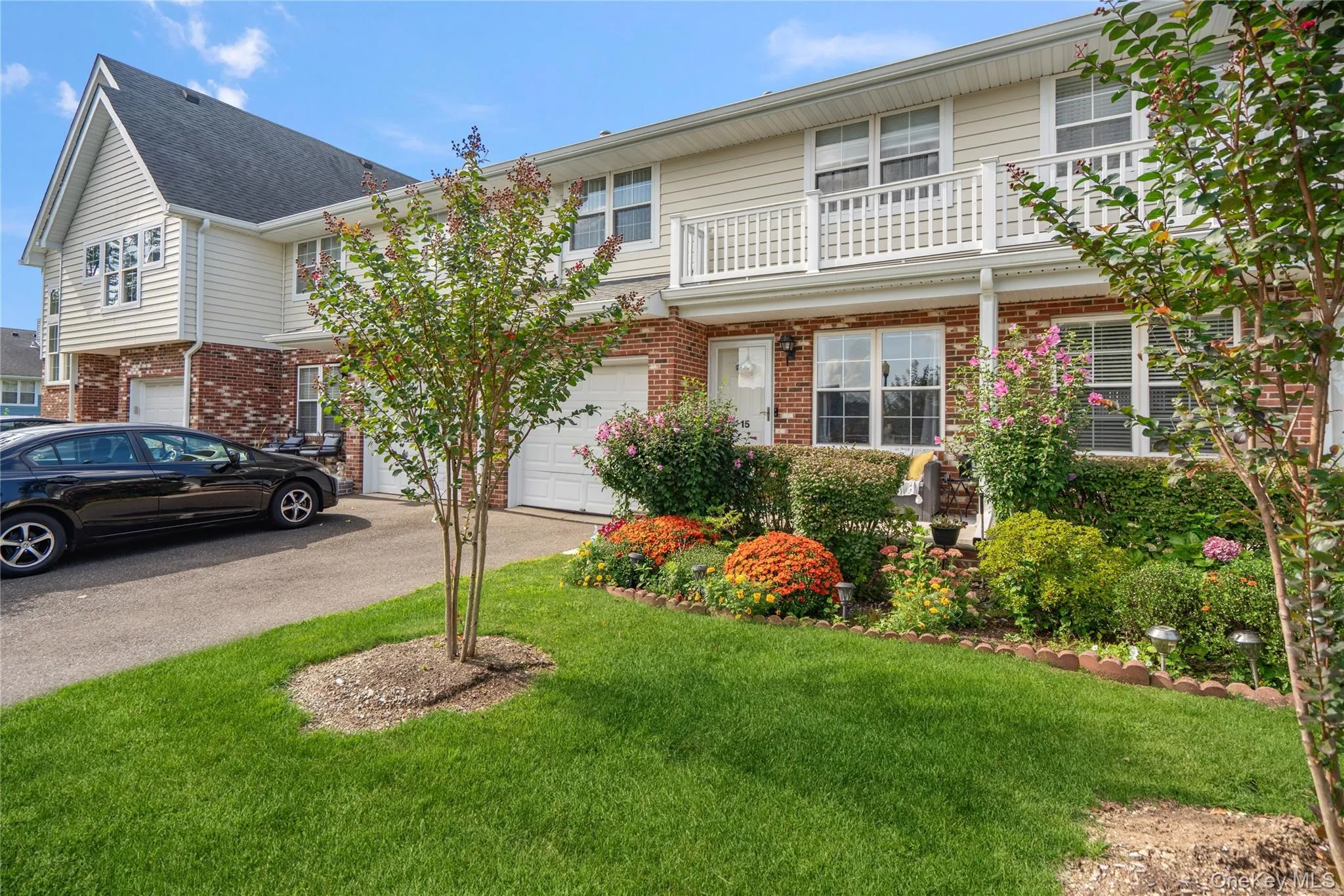 Exterior featuring brick and siding facade, an upper-level balcony with white railing, integrated garage, and a well-maintained front lawn with mature landscaping Exterior featuring brick and siding facade, an upper-level balcony with white railing, integrated garage, and a well-maintained front lawn with mature landscaping