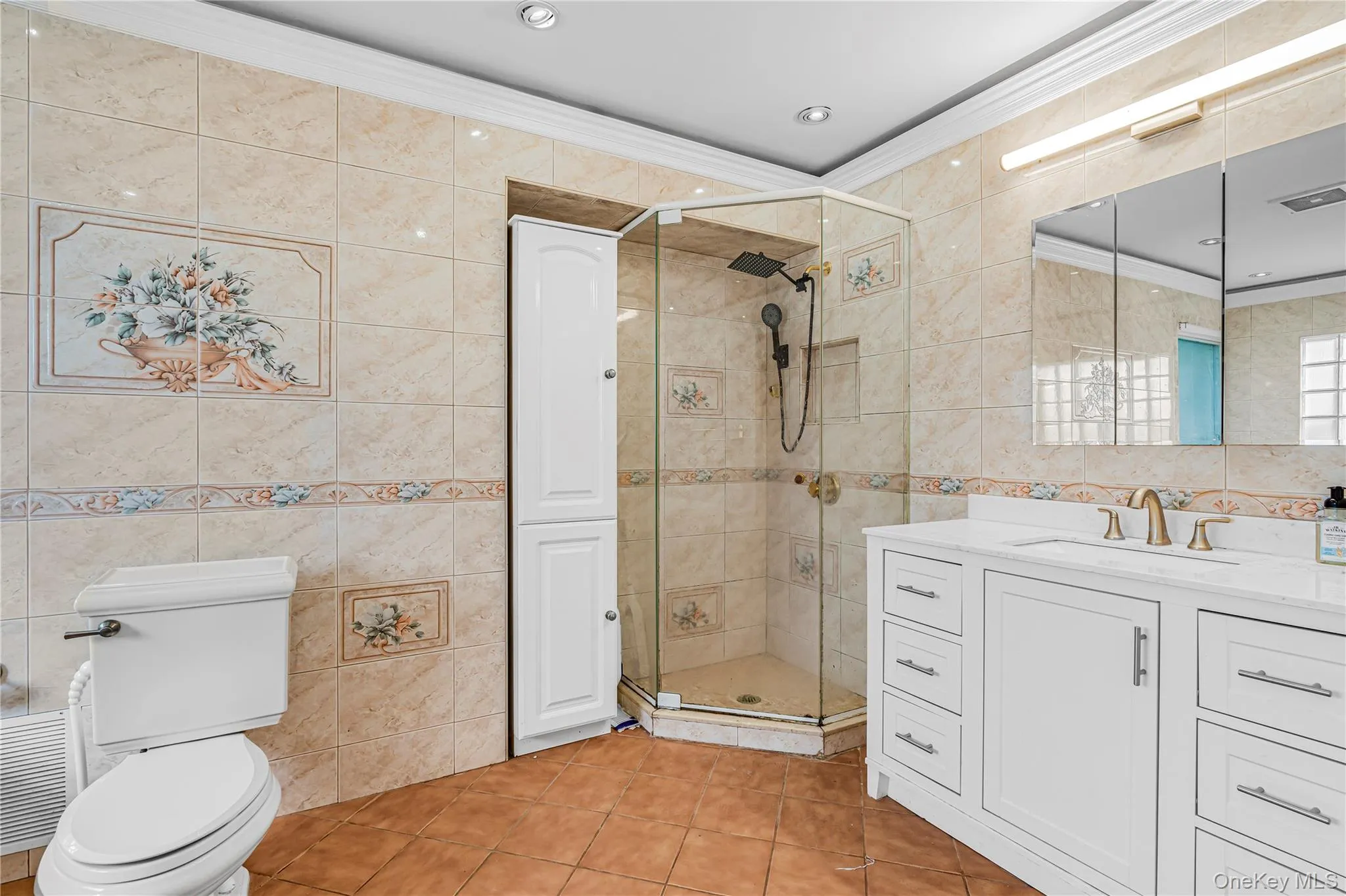 Tiled bathroom featuring a glass-enclosed shower, white vanity with integrated sink, gold-tone fixtures, and recessed lighting Tiled bathroom featuring a glass-enclosed shower, white vanity with integrated sink, gold-tone fixtures, and recessed lighting