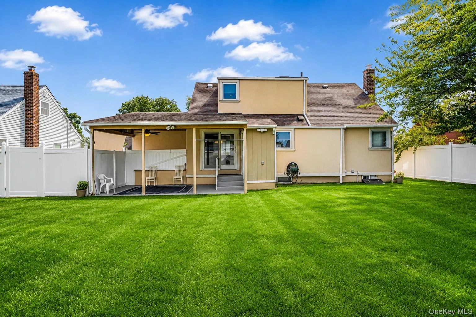 Expansive backyard with a manicured lawn, a covered patio, and white privacy fencing Expansive backyard with a manicured lawn, a covered patio, and white privacy fencing