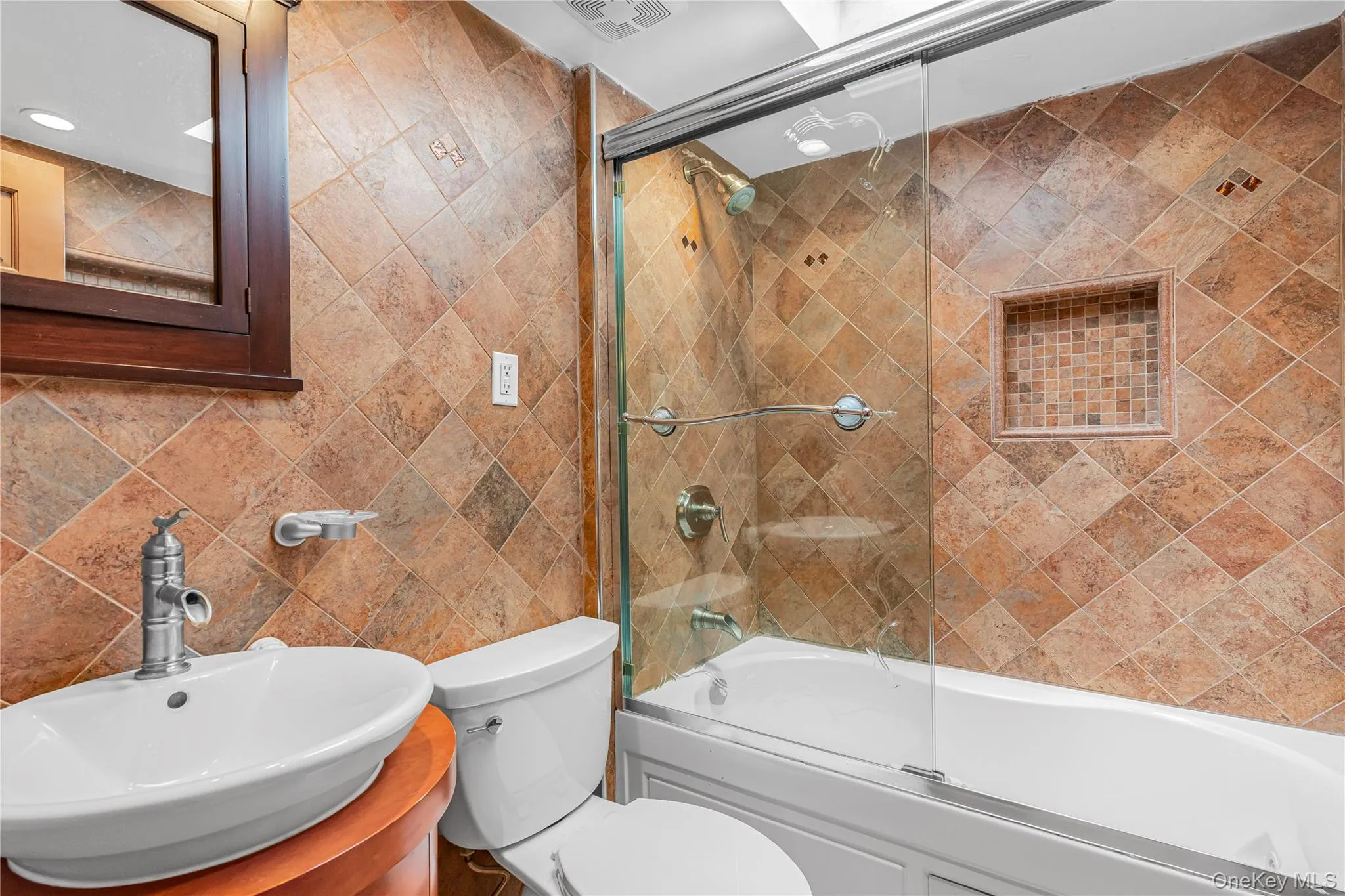 Full tile-surround bath with glass sliding door, integrated shower niche, and a vessel sink on a wood-finish vanity Full tile-surround bath with glass sliding door, integrated shower niche, and a vessel sink on a wood-finish vanity