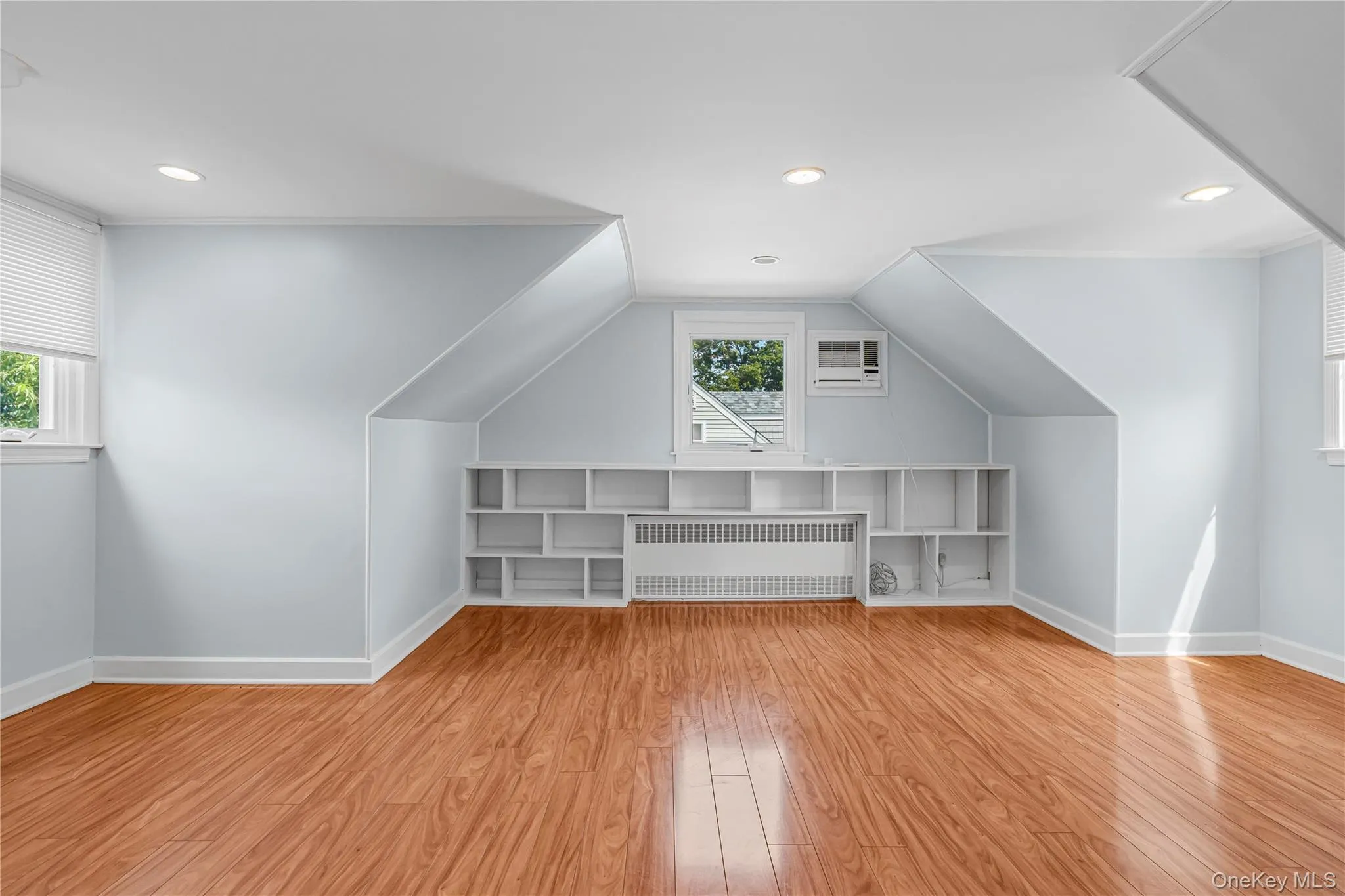 Wood-finish flooring with recessed lighting, built-in shelving, and a window air conditioning unit Wood-finish flooring with recessed lighting, built-in shelving, and a window air conditioning unit