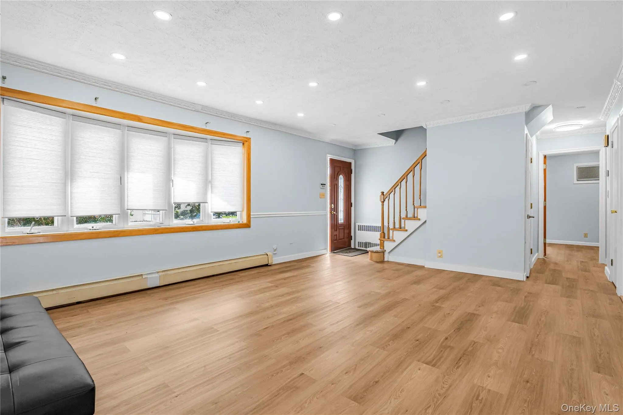 Spacious living area featuring wood-finish flooring, recessed lighting, and a large window with natural wood trim Spacious living area featuring wood-finish flooring, recessed lighting, and a large window with natural wood trim