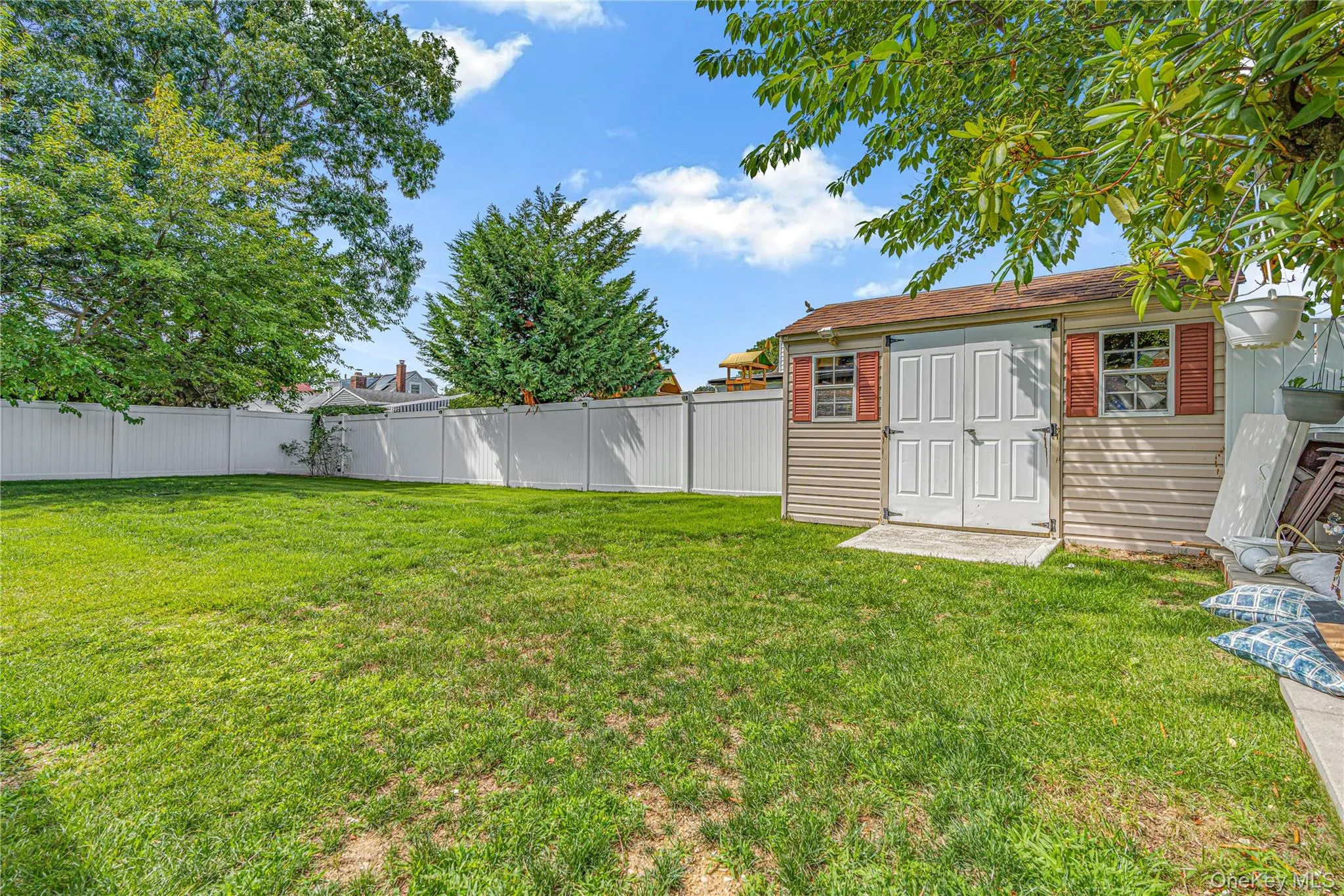 Expansive grassy yard with white privacy fencing and a utility shed featuring red shutters Expansive grassy yard with white privacy fencing and a utility shed featuring red shutters