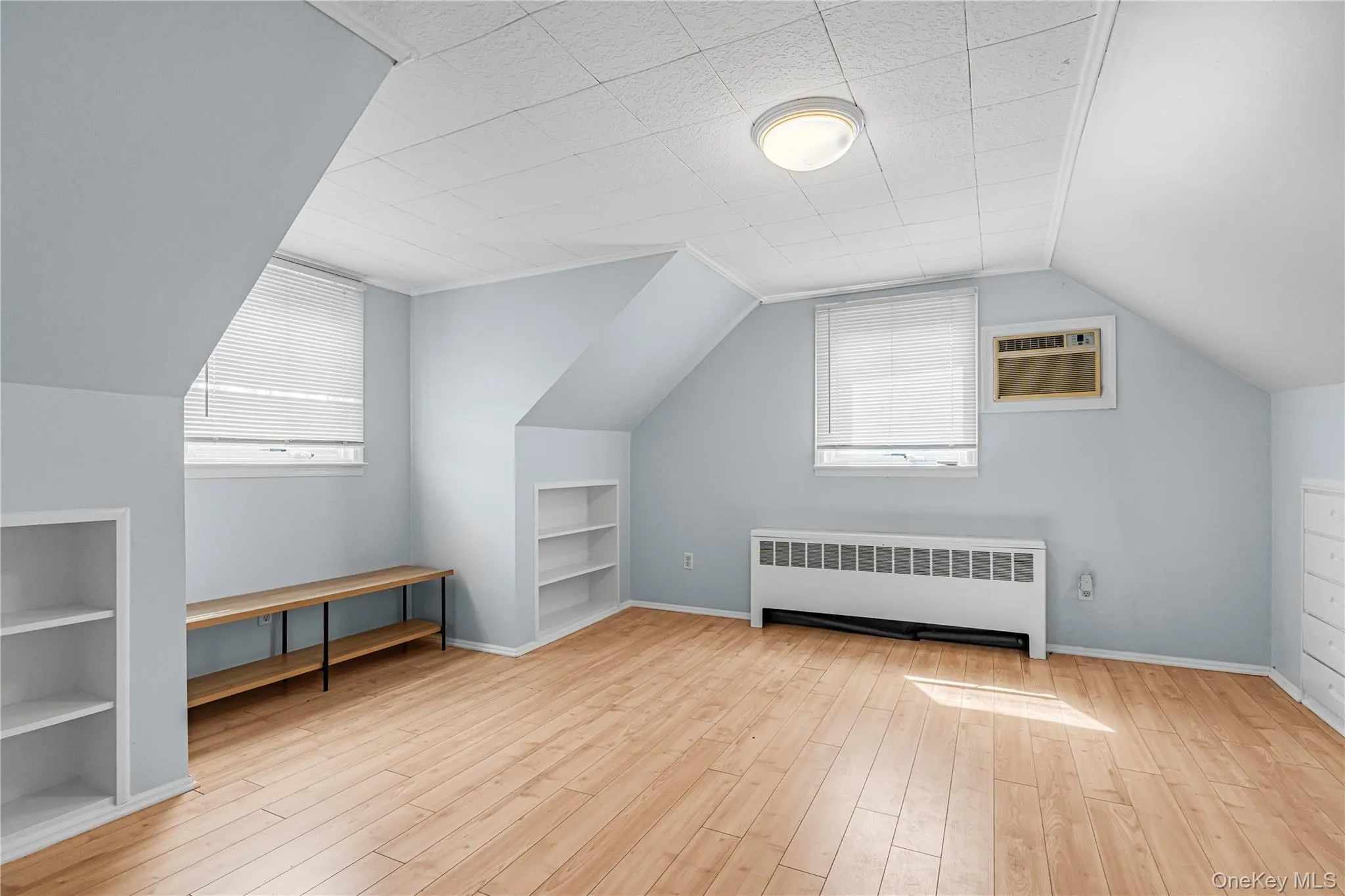 Wood-finish flooring, built-in shelving, two windows with blinds, and a flush mount ceiling light Wood-finish flooring, built-in shelving, two windows with blinds, and a flush mount ceiling light