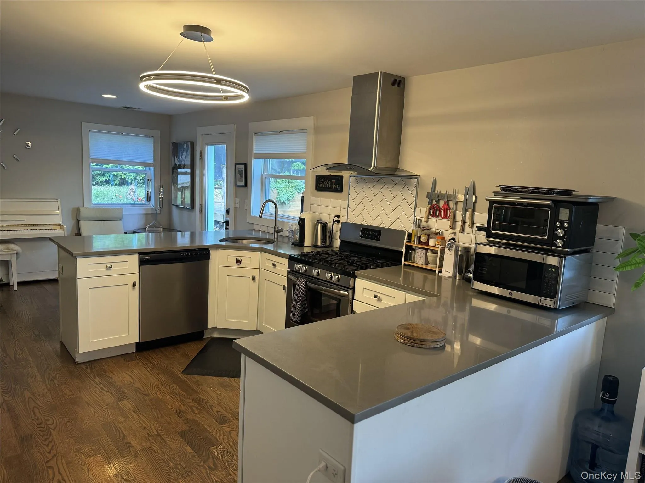 Kitchen with a peninsula, stainless steel appliances, wall chimney range hood, dark wood finished floors, and decorative backsplash Kitchen with a peninsula, stainless steel appliances, wall chimney range hood, dark wood finished floors, and decorative backsplash