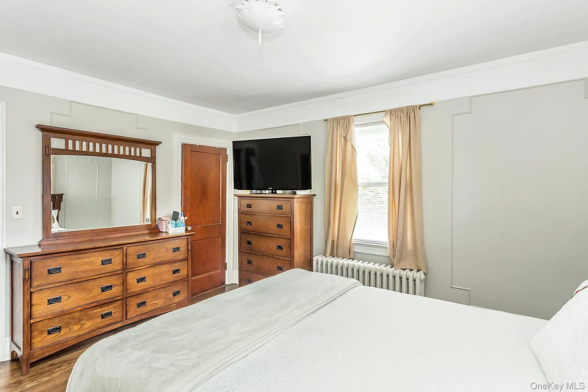 Wood-finish flooring, crown molding, and a window with a radiator below Wood-finish flooring, crown molding, and a window with a radiator below