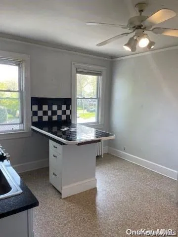Built-in kitchen island with drawer storage, black and white tiled backsplash, ceiling fan with integrated lighting, and dual window exposures Built-in kitchen island with drawer storage, black and white tiled backsplash, ceiling fan with integrated lighting, and dual window exposures