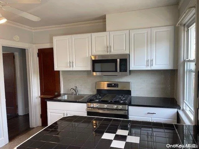 Kitchen featuring white upper and lower cabinetry, stainless steel appliances, black Quartz countertops, and a light-colored tile backsplash Kitchen featuring white upper and lower cabinetry, stainless steel appliances, black Quartz countertops, and a light-colored tile backsplash