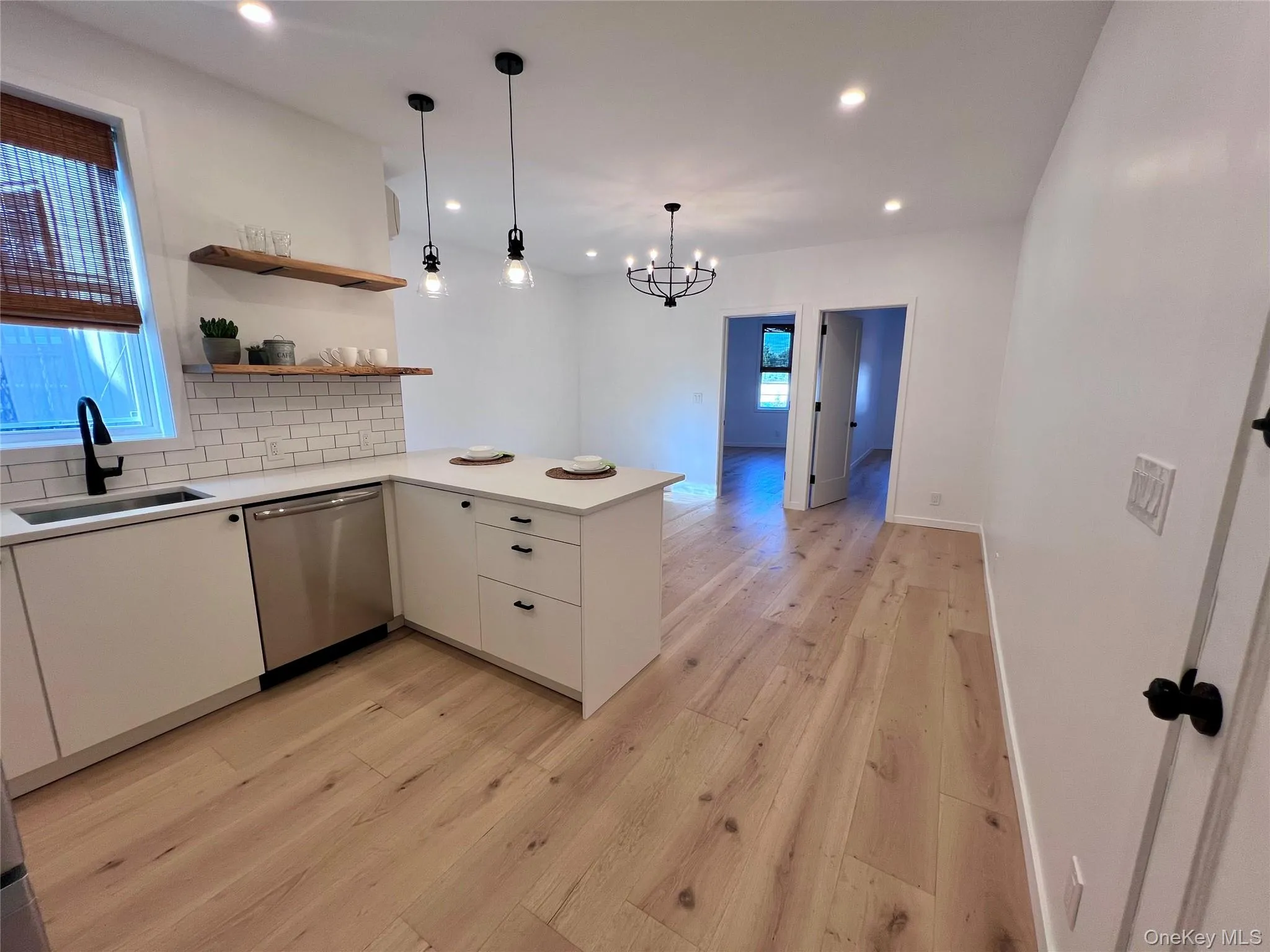 Kitchen with white shaker cabinetry, stainless steel dishwasher, white subway tile backsplash, and wood-finish flooring Kitchen with white shaker cabinetry, stainless steel dishwasher, white subway tile backsplash, and wood-finish flooring
