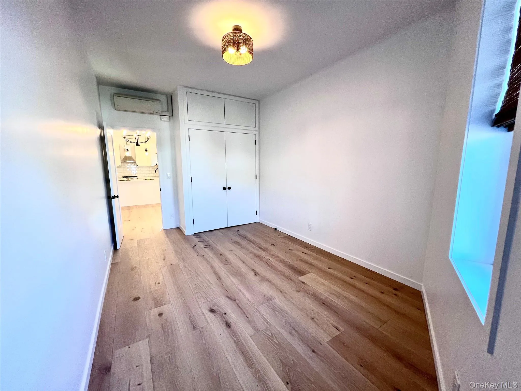Wood-finish flooring throughout, featuring a built-in closet with upper cabinetry, a recessed wall niche, and a contemporary ceiling fixture Wood-finish flooring throughout, featuring a built-in closet with upper cabinetry, a recessed wall niche, and a contemporary ceiling fixture