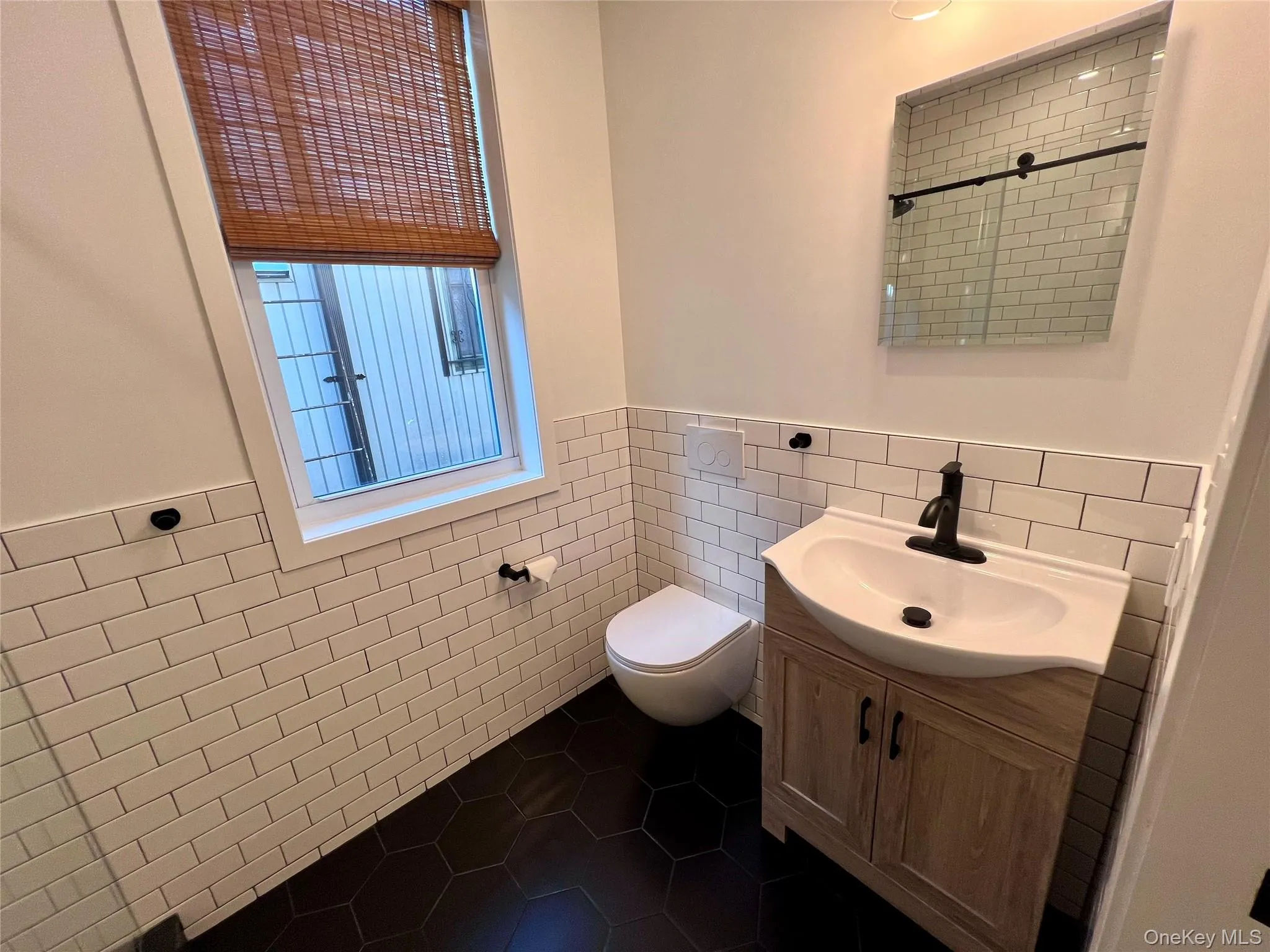 Bathroom featuring black hexagonal floor tiles, subway tile wainscoting, and a wood-finish vanity with a black faucet Bathroom featuring black hexagonal floor tiles, subway tile wainscoting, and a wood-finish vanity with a black faucet