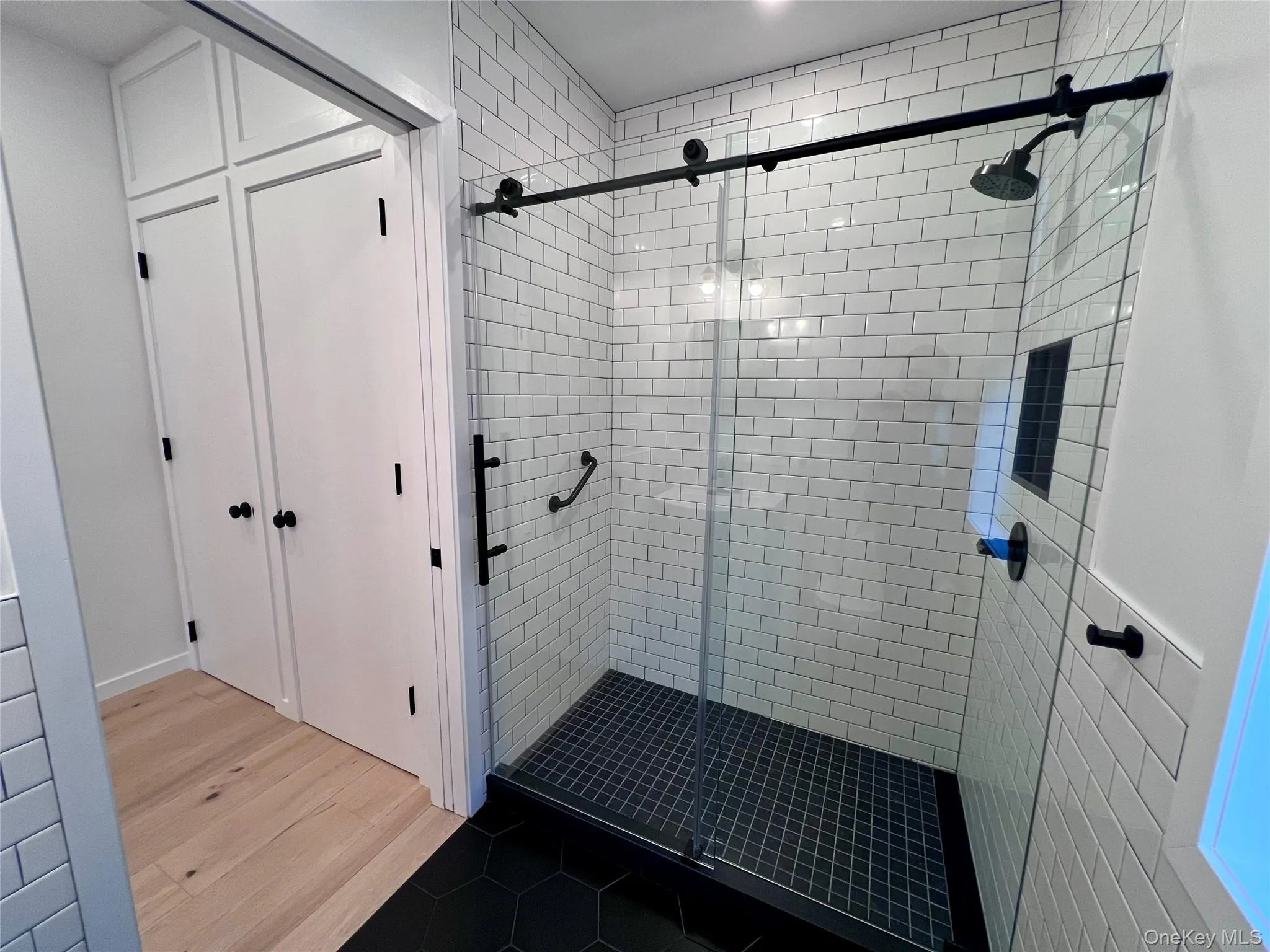 Glass-enclosed shower with subway tile walls, a dark hexagonal tile floor, and black fixtures Glass-enclosed shower with subway tile walls, a dark hexagonal tile floor, and black fixtures