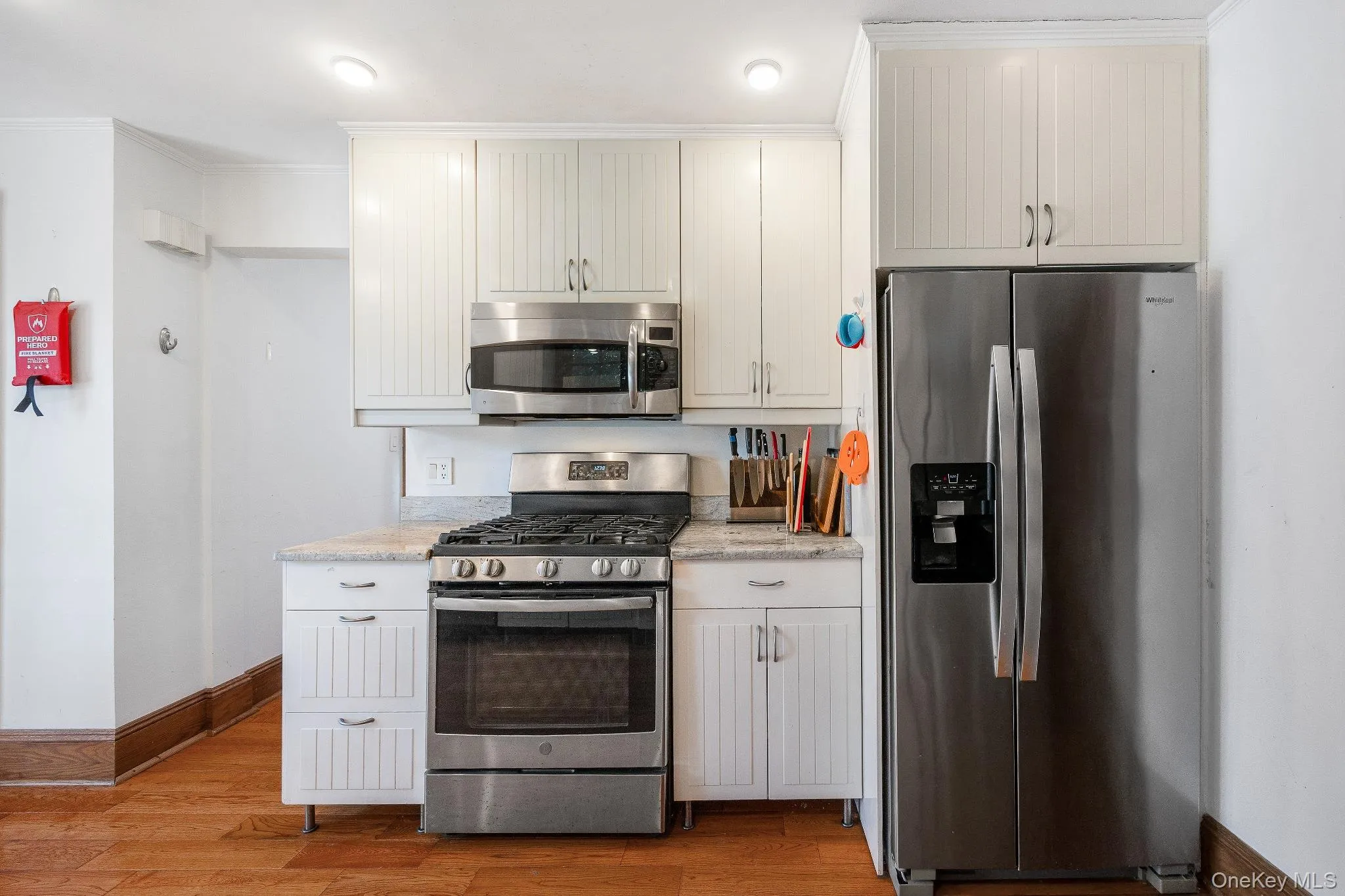 Kitchen featuring appliances with stainless steel finishes, light wood-type flooring, crown molding, and light stone counters Kitchen featuring appliances with stainless steel finishes, light wood-type flooring, crown molding, and light stone counters
