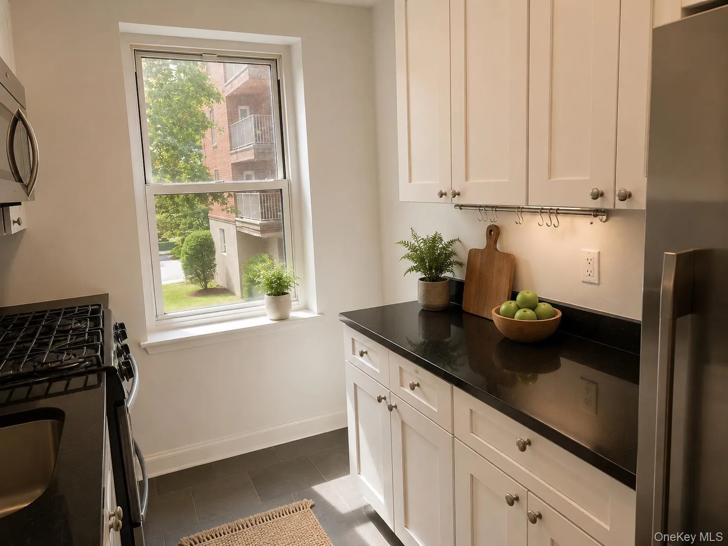White shaker cabinetry with dark countertops, stainless steel appliances, and dark tile flooring White shaker cabinetry with dark countertops, stainless steel appliances, and dark tile flooring