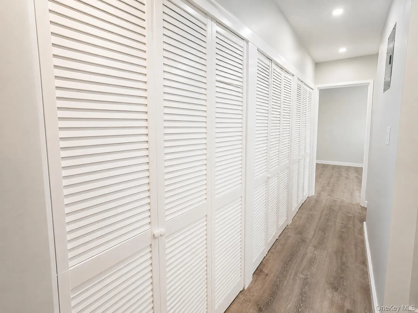 Hallway featuring extensive louvered bifold doors, vinyl -finish flooring, recessed lighting, and light gray wall paint Hallway featuring extensive louvered bifold doors, vinyl -finish flooring, recessed lighting, and light gray wall paint