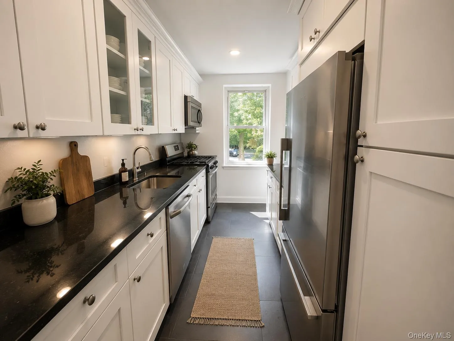 Galley kitchen featuring white shaker cabinetry, dark countertops, stainless steel appliances, and dark tile flooring Galley kitchen featuring white shaker cabinetry, dark countertops, stainless steel appliances, and dark tile flooring