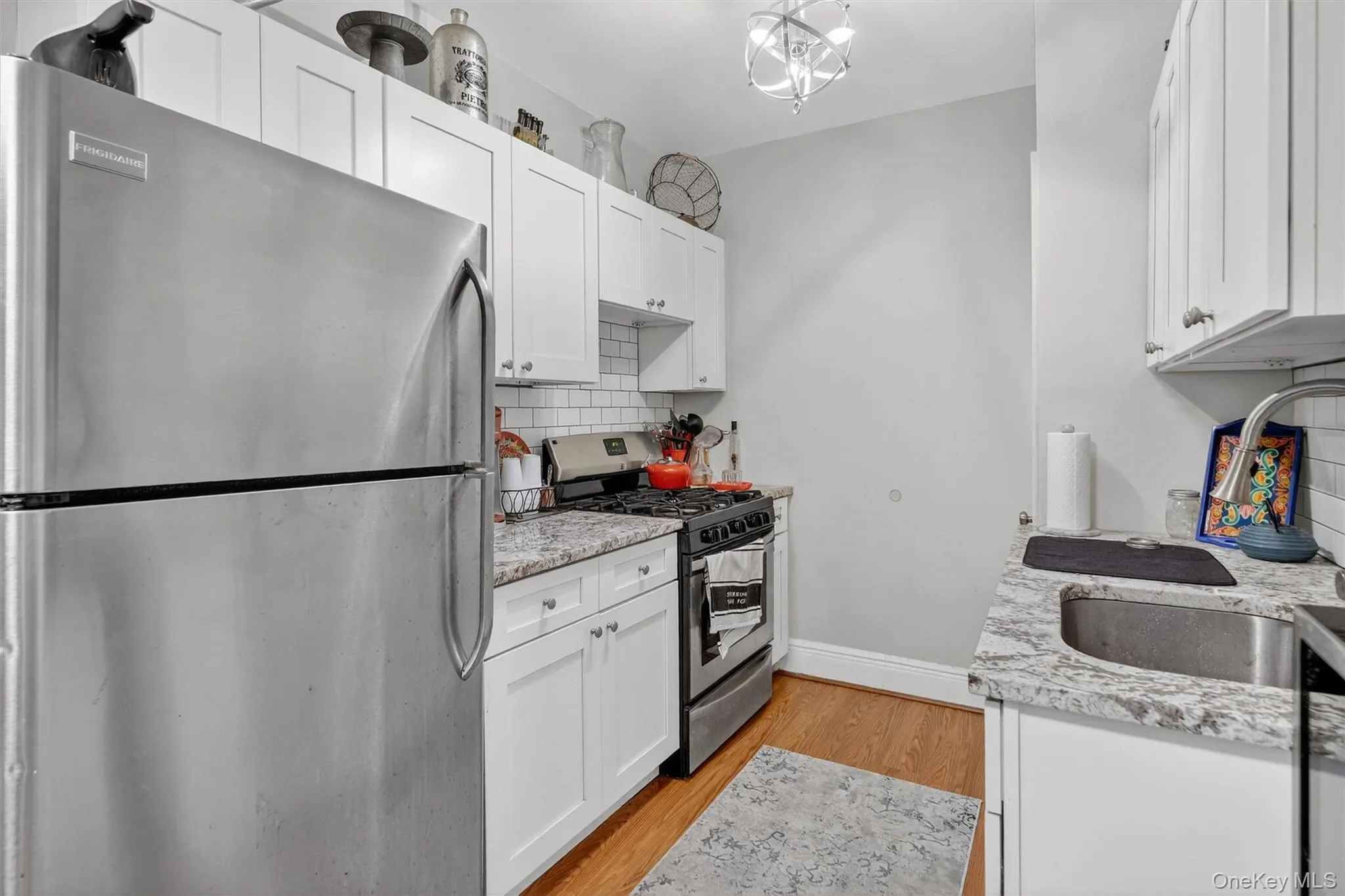 Kitchen with stainless steel appliances, white cabinets, light wood finished floors, and light stone countertops Kitchen with stainless steel appliances, white cabinets, light wood finished floors, and light stone countertops