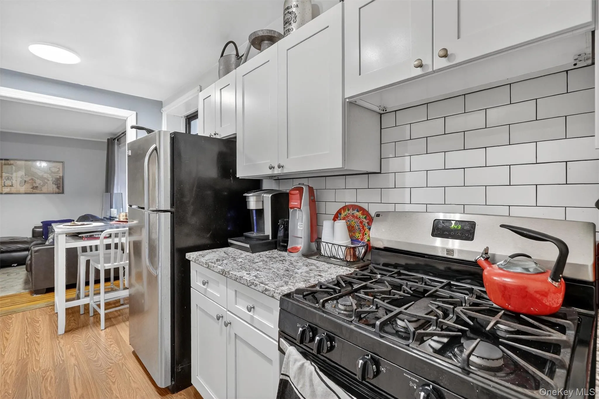 Kitchen with appliances with stainless steel finishes, white cabinets, backsplash, and light wood-style floors Kitchen with appliances with stainless steel finishes, white cabinets, backsplash, and light wood-style floors