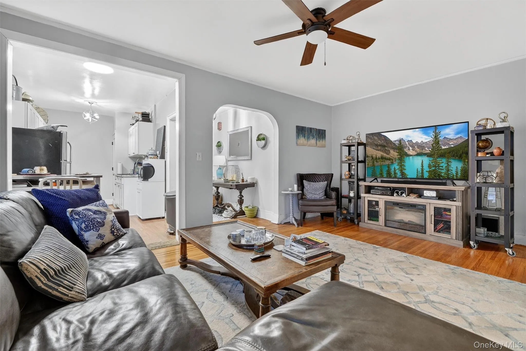 Living area featuring arched walkways, light wood-style floors, and a ceiling fan Living area featuring arched walkways, light wood-style floors, and a ceiling fan