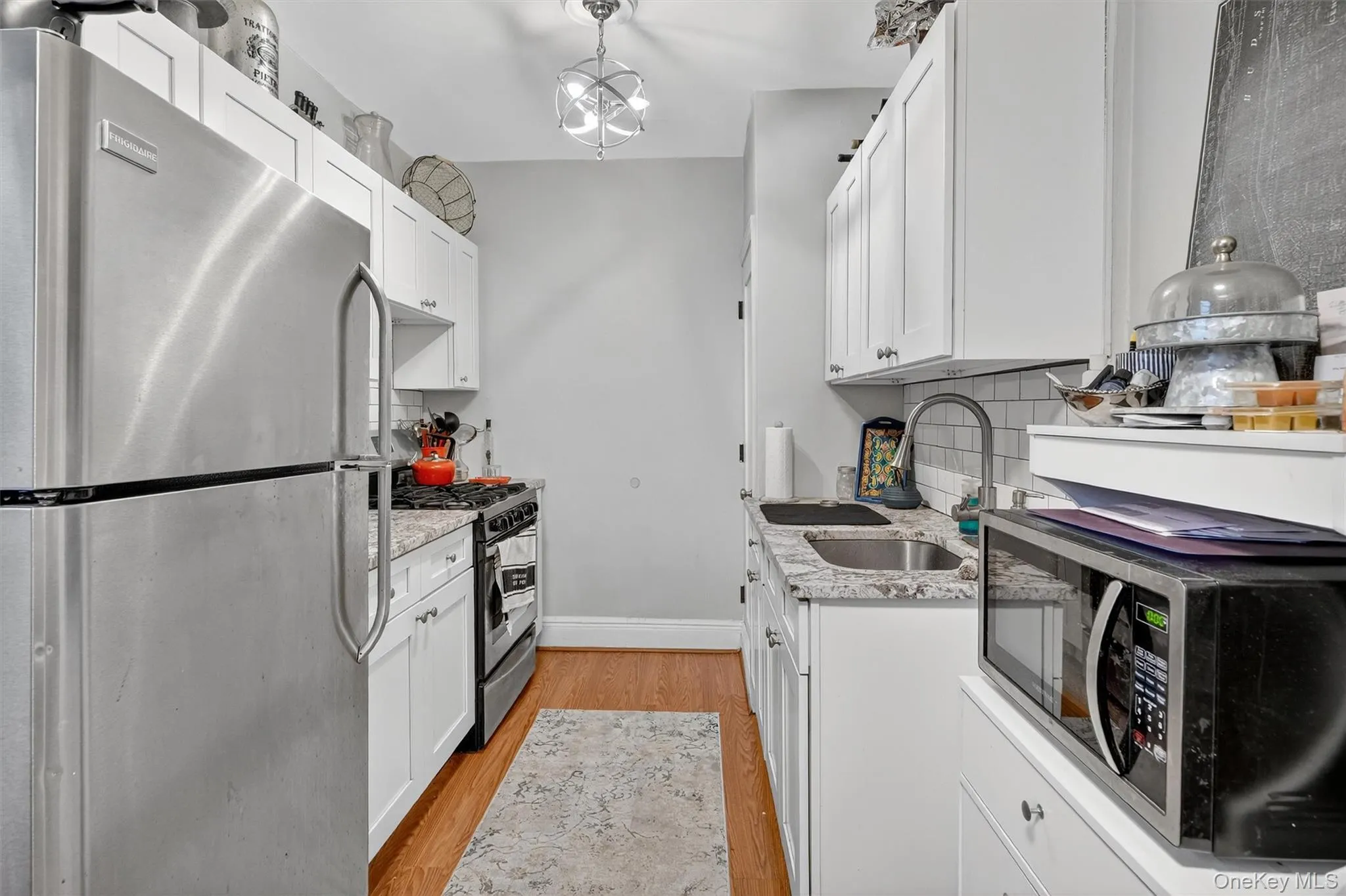 Kitchen featuring stainless steel appliances, light stone counters, white cabinets, light wood-style flooring, and decorative backsplash Kitchen featuring stainless steel appliances, light stone counters, white cabinets, light wood-style flooring, and decorative backsplash