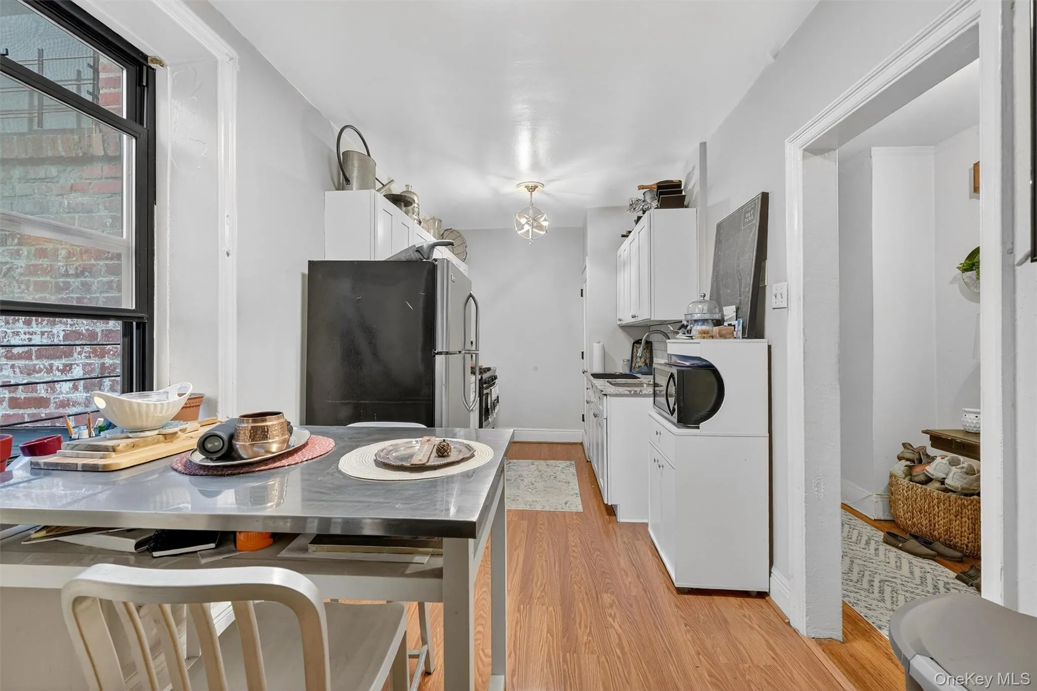 Kitchen with white cabinetry, freestanding refrigerator, light wood-style floors, and black microwave Kitchen with white cabinetry, freestanding refrigerator, light wood-style floors, and black microwave