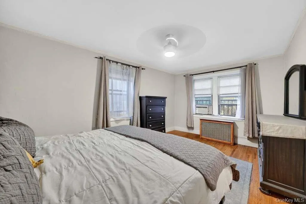 Bedroom featuring light wood-type flooring, radiator heating unit, ornamental molding, and a ceiling fan Bedroom featuring light wood-type flooring, radiator heating unit, ornamental molding, and a ceiling fan