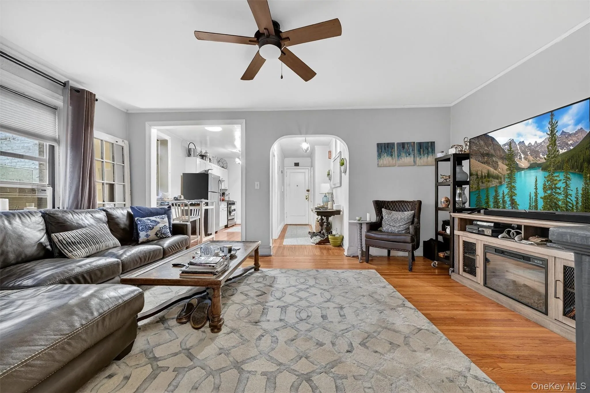 Living area featuring arched walkways, light wood-style floors, a ceiling fan, ornamental molding, and cooling unit Living area featuring arched walkways, light wood-style floors, a ceiling fan, ornamental molding, and cooling unit