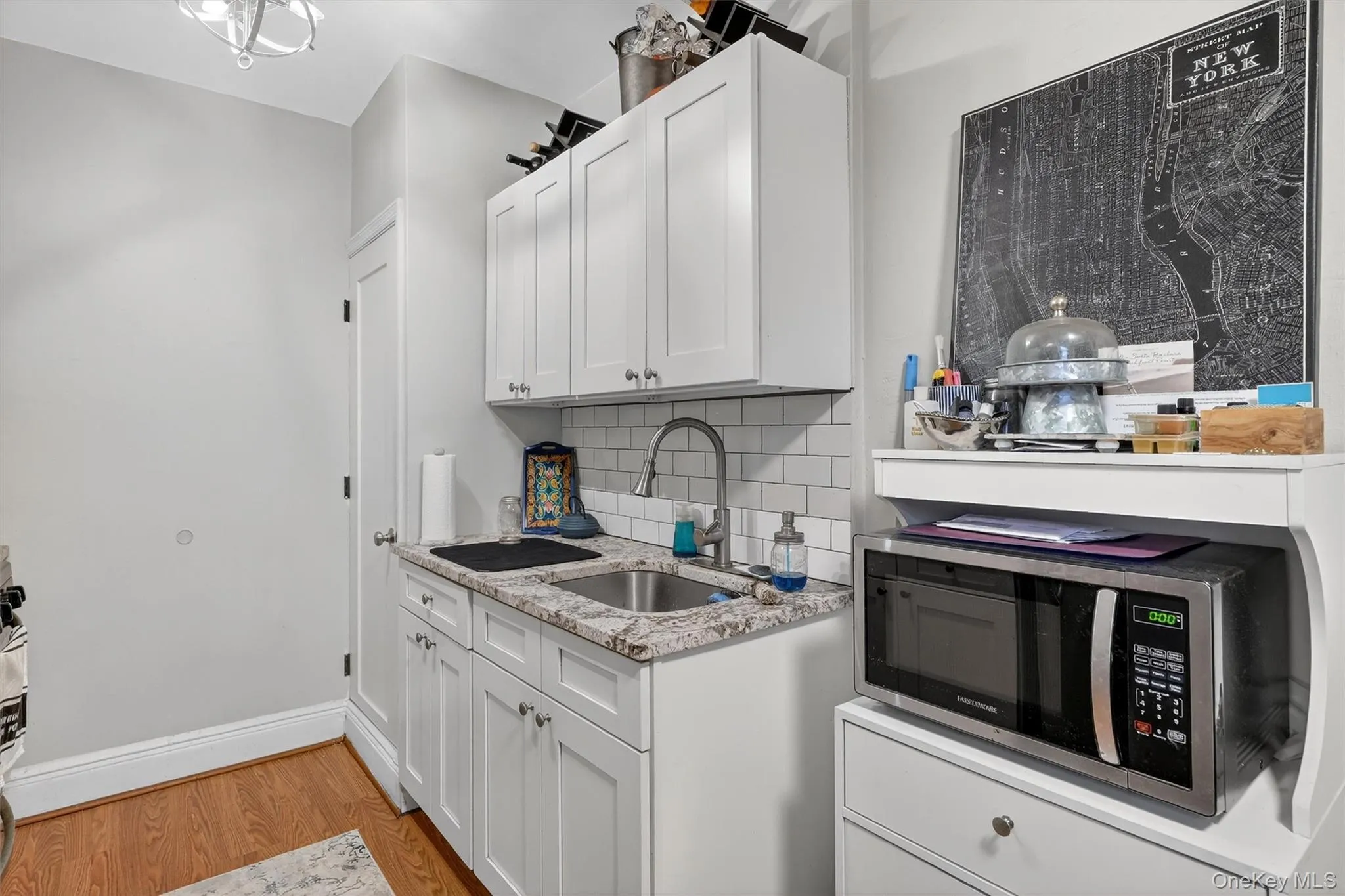 Kitchen featuring white cabinets, light wood-type flooring, tasteful backsplash, light stone countertops, and stainless steel microwave Kitchen featuring white cabinets, light wood-type flooring, tasteful backsplash, light stone countertops, and stainless steel microwave
