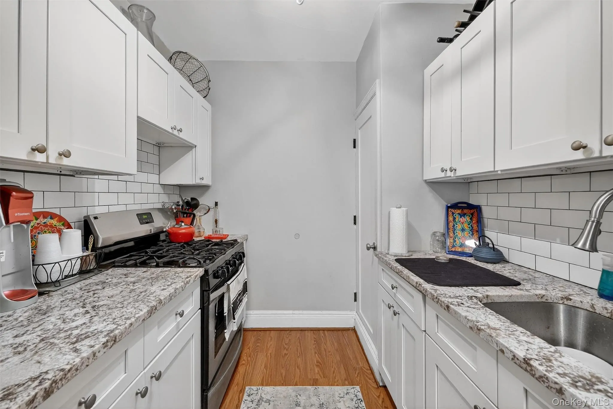 Kitchen with stainless steel range with gas cooktop, white cabinets, light wood-type flooring, and light stone countertops Kitchen with stainless steel range with gas cooktop, white cabinets, light wood-type flooring, and light stone countertops