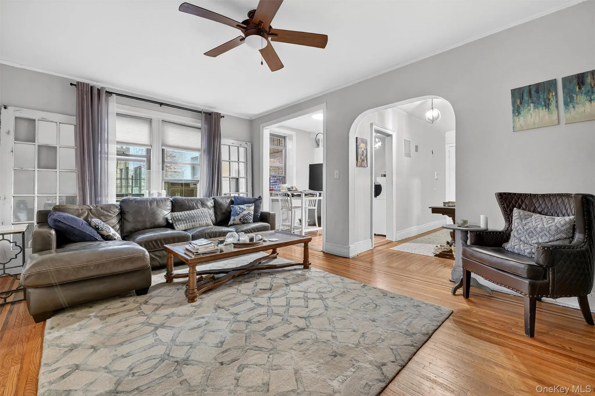 Living area featuring ornamental molding, arched walkways, ceiling fan, and light wood-style flooring Living area featuring ornamental molding, arched walkways, ceiling fan, and light wood-style flooring