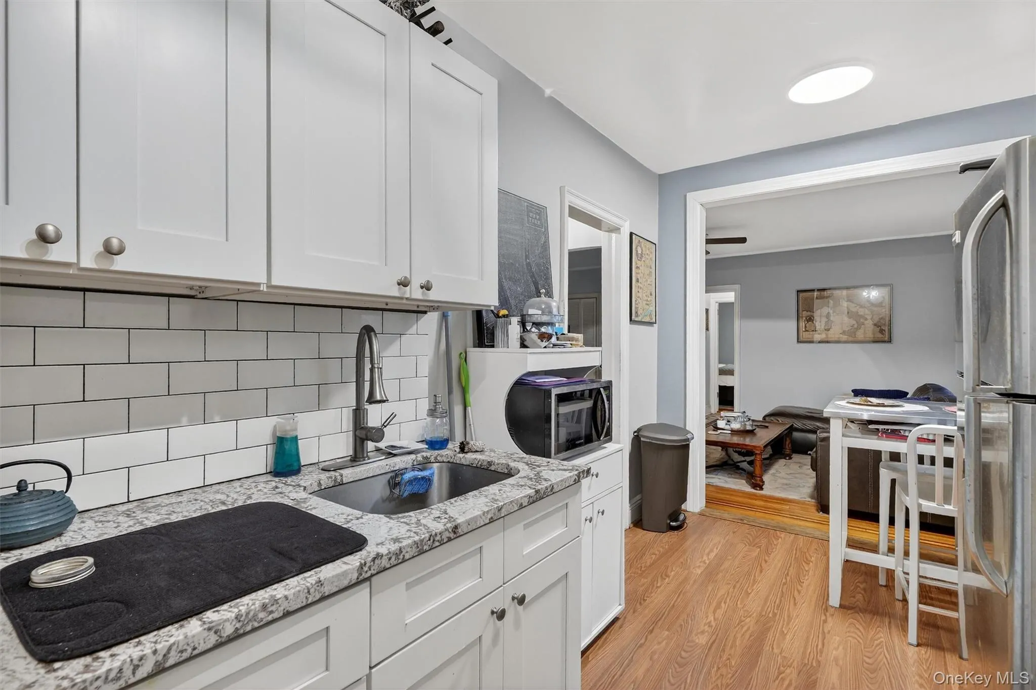 Kitchen featuring light stone counters, white cabinets, backsplash, freestanding refrigerator, and light wood-style floors Kitchen featuring light stone counters, white cabinets, backsplash, freestanding refrigerator, and light wood-style floors