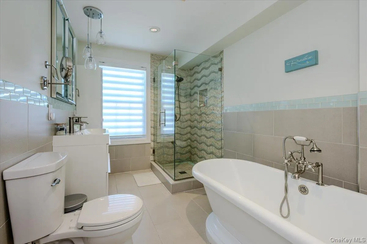 Spa-inspired primary bathroom featuring a freestanding soaking tub with deck-mounted fixtures, a walk-in shower enclosure with geometric tile surround and rainfall showerhead, dual vanities with vessel sinks, and natural light from casement windows Spa-inspired primary bathroom featuring a freestanding soaking tub with deck-mounted fixtures, a walk-in shower enclosure with geometric tile surround and rainfall showerhead, dual vanities with vessel sinks, and natural light from casement windows