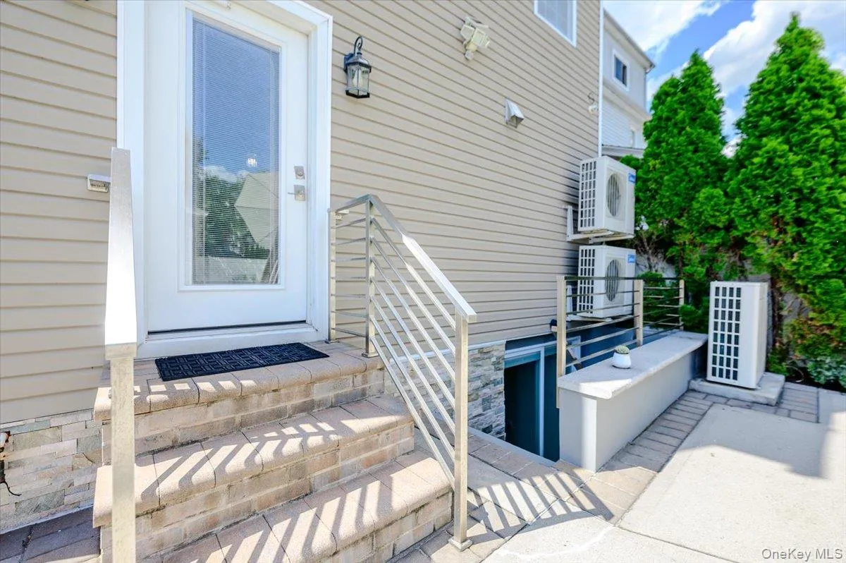 Welcoming entry featuring a white-framed glass door with sidelights, brick-accented foundation steps with metal railings, and vinyl siding exterior Welcoming entry featuring a white-framed glass door with sidelights, brick-accented foundation steps with metal railings, and vinyl siding exterior