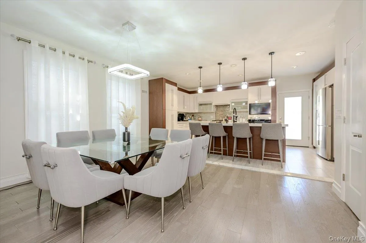 Modern light wood-finish flooring, square chandelier, white kitchen cabinetry, kitchen island with seating, pendant lighting Modern light wood-finish flooring, square chandelier, white kitchen cabinetry, kitchen island with seating, pendant lighting