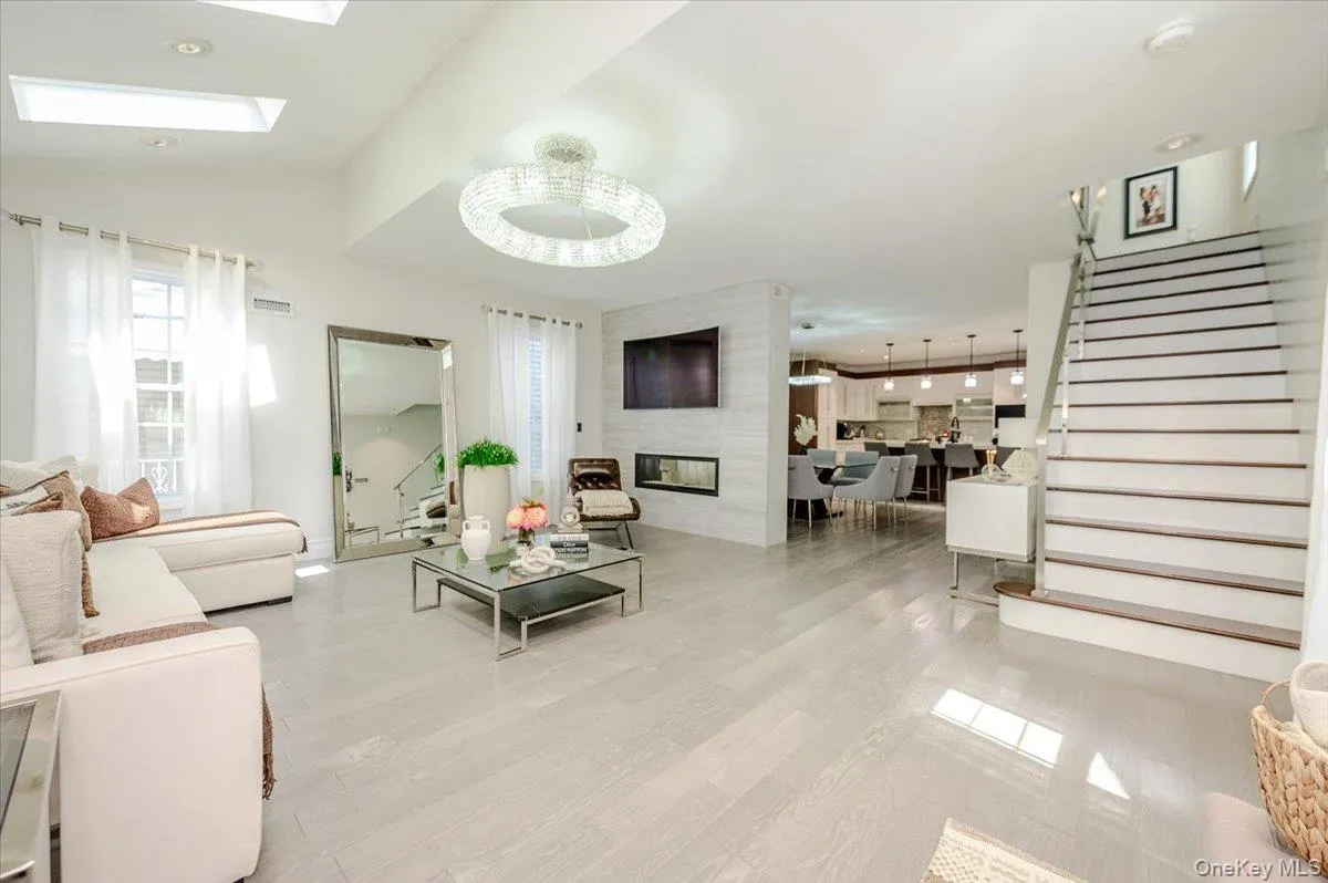 High ceilings with skylights, light wood-finish flooring, staircase with partial glass railing, built-in fireplace, and a contemporary chandelier High ceilings with skylights, light wood-finish flooring, staircase with partial glass railing, built-in fireplace, and a contemporary chandelier