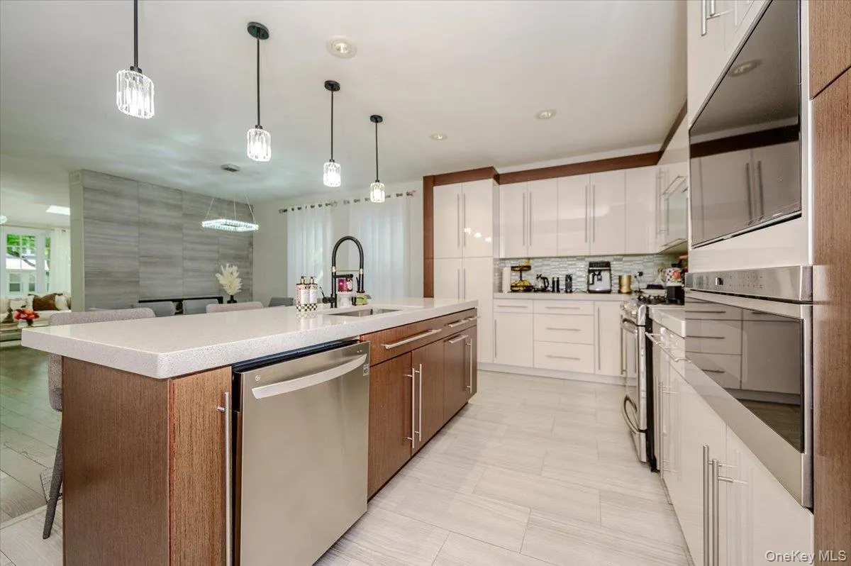 Gourmet kitchen with an expansive quartz island, stainless steel appliances, modern pendant lighting, a tile backsplash, and light wood-finish cabinetry Gourmet kitchen with an expansive quartz island, stainless steel appliances, modern pendant lighting, a tile backsplash, and light wood-finish cabinetry
